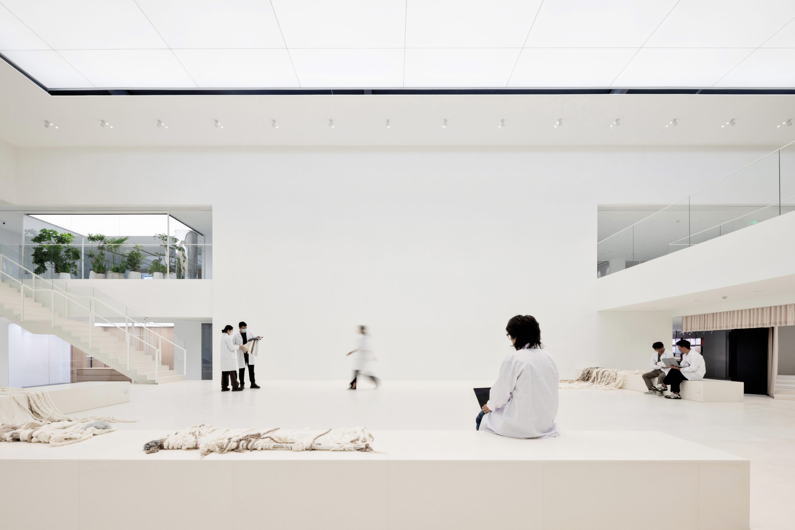 Inside the Erdos Cashmere Centre, six figures in white lab coats sit on white benches and stand around inside an all-white workplace interior, facing an expansive white wall.