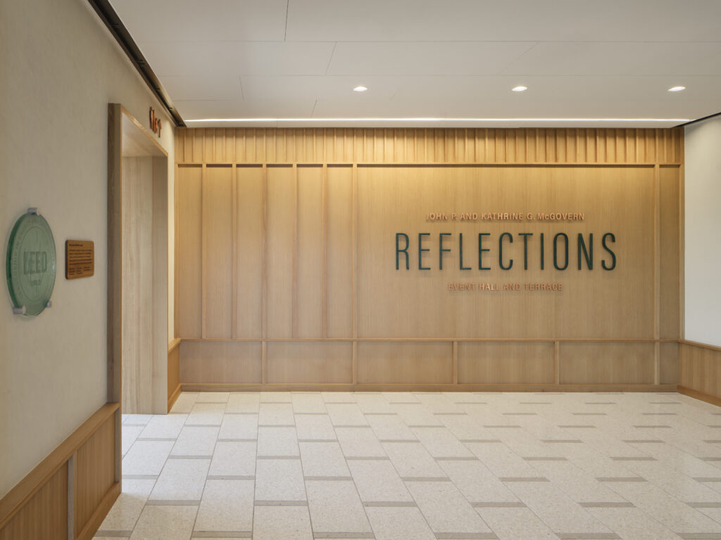 A hallway with a wood-paneled wall featuring the words “Reflections Event Hall and Terrace” in large letters and a LEED certification plaque mounted on the left wall, reminiscent of the sophisticated design elements seen at the Lucas Museum of Narrative Art.