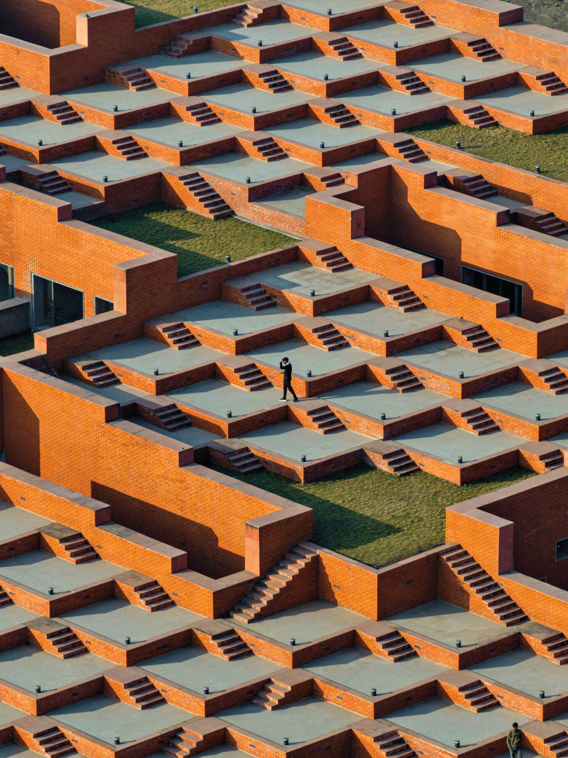 A person walking across a series of stepped, red-brick terraces with gray concrete surfaces and stairways.