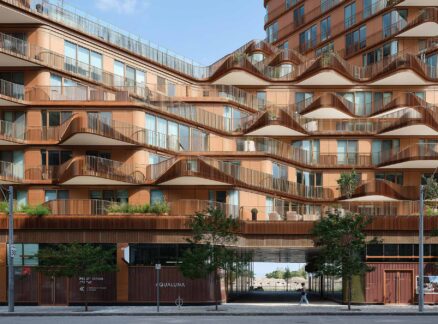 Modern apartment building by 3XN with wavy balconies, large windows, ground-floor shops, and trees lining the sidewalk.