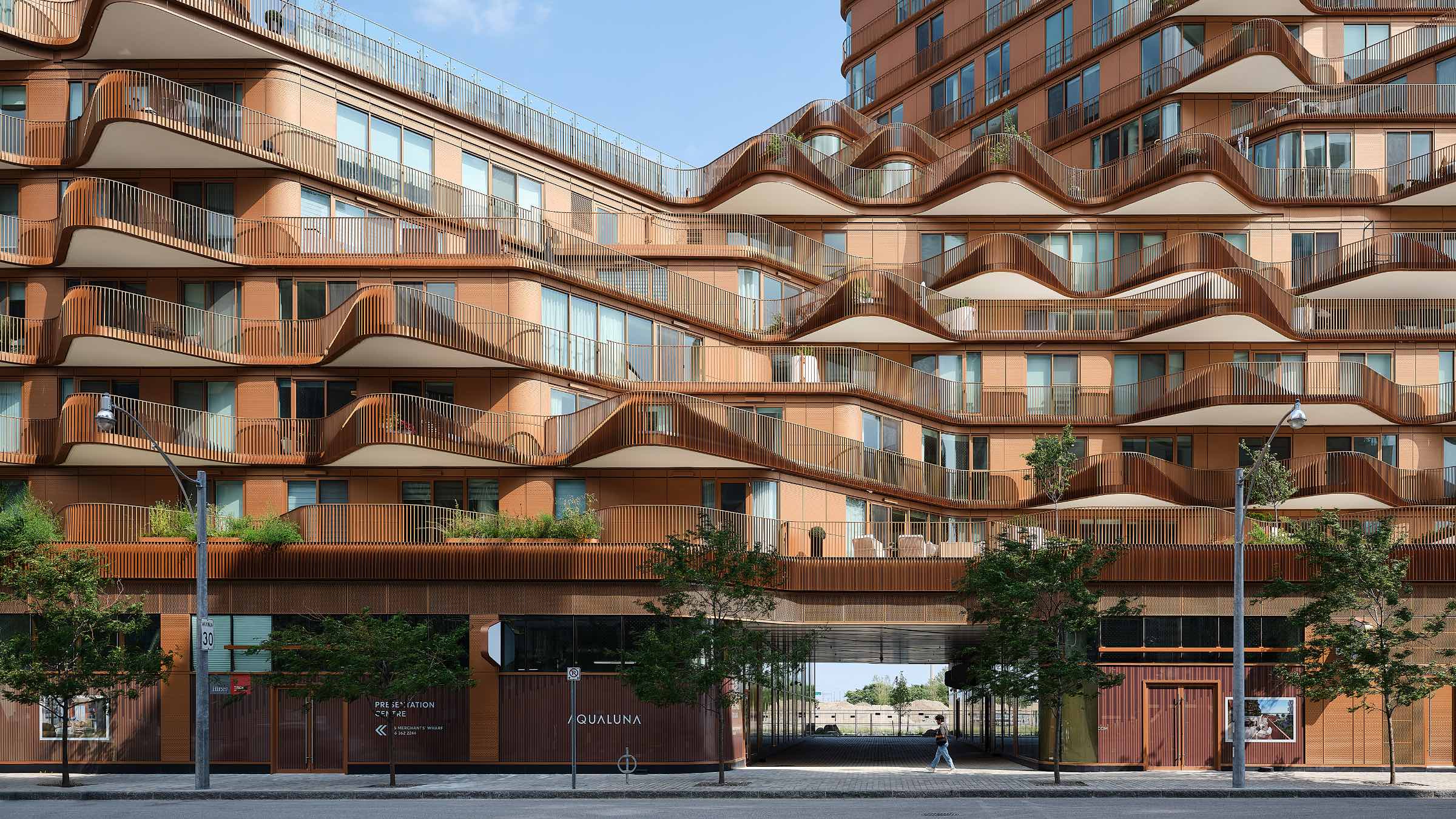 Modern apartment building by 3XN with wavy balconies, large windows, ground-floor shops, and trees lining the sidewalk.