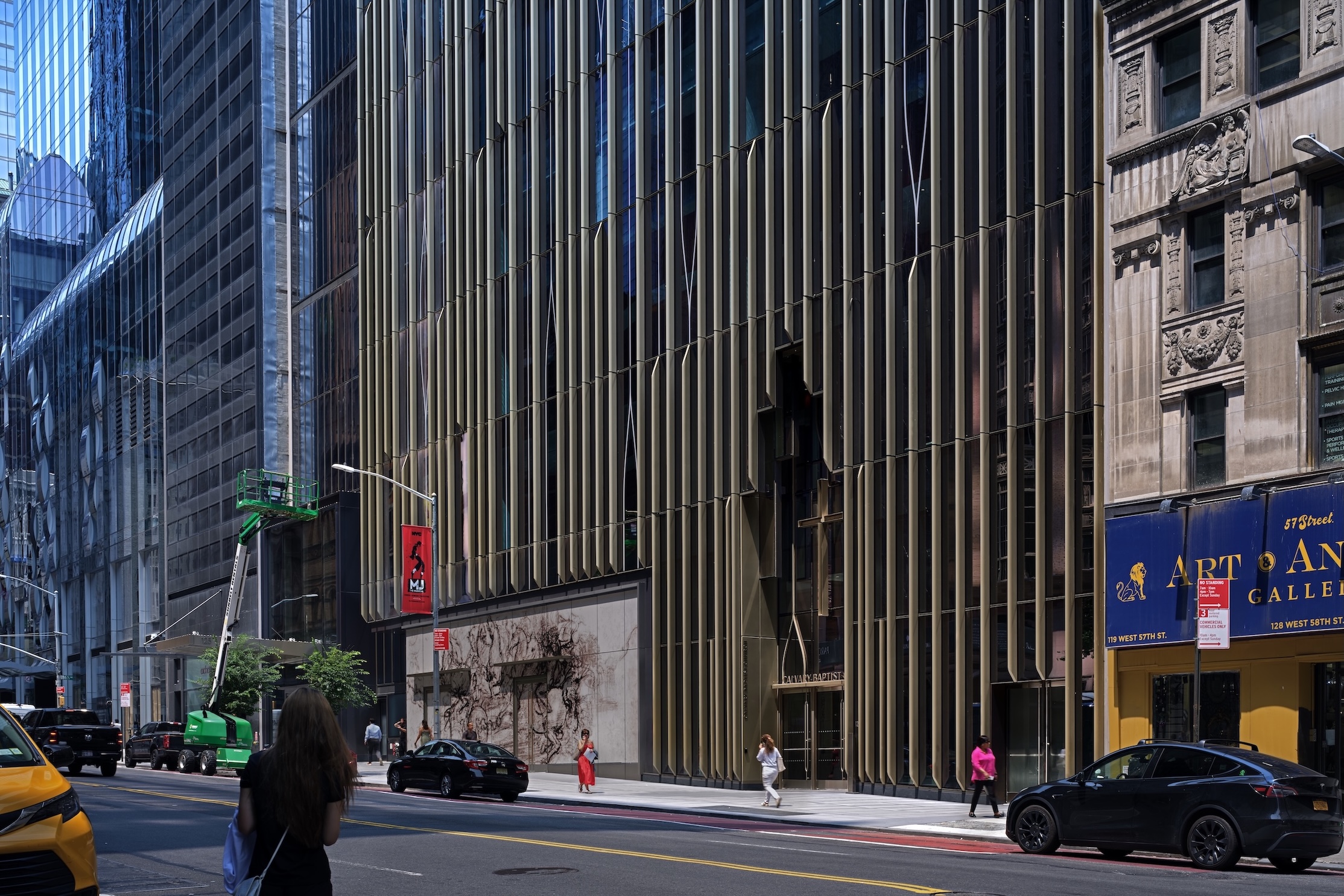 The Calvary Baptist Church on West 57th Street in New York City, featuring a modern bronze-toned vertical facade reminiscent of the sleek lines found at the Lucas Museum of Narrative Art, with pedestrians and vehicles on the street in front.