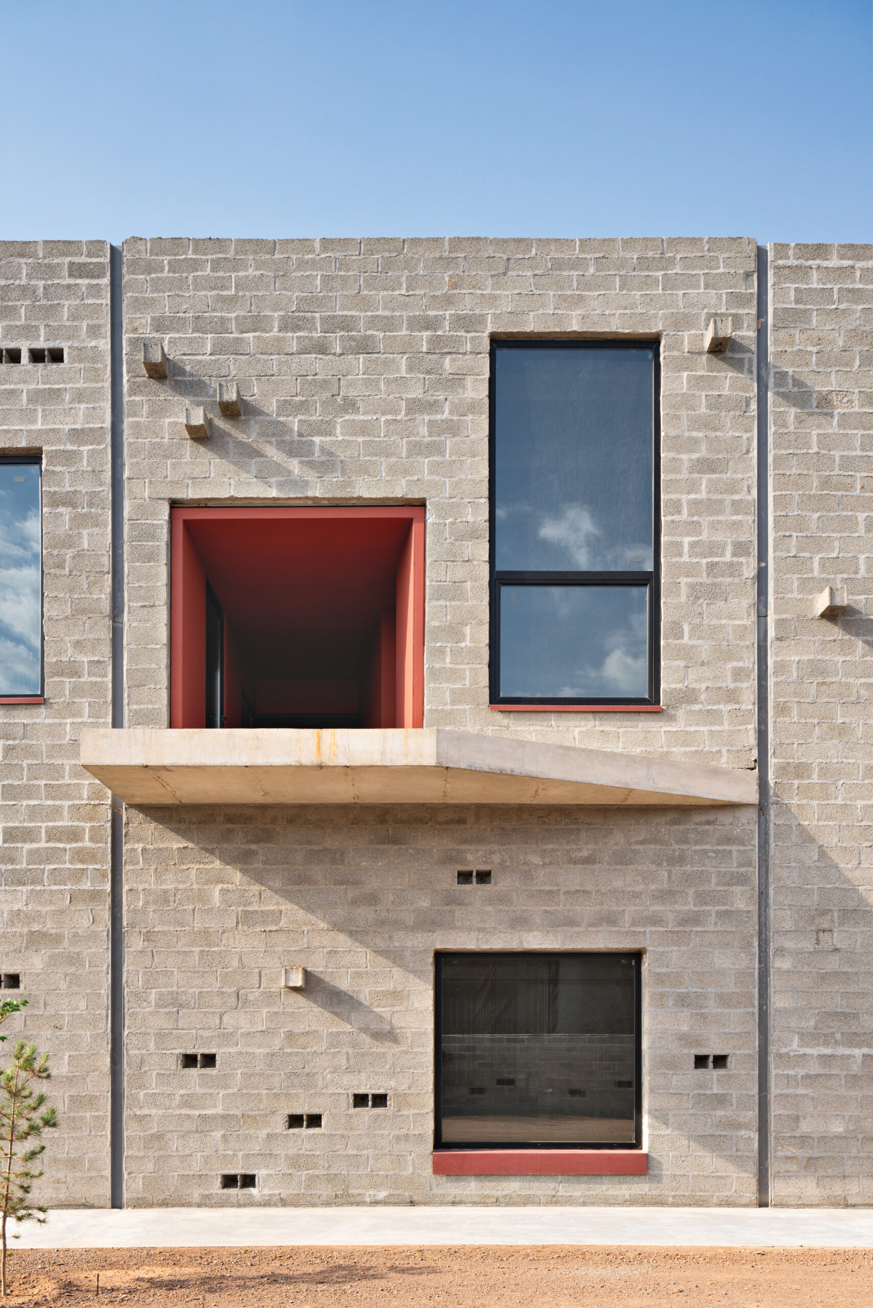 A close-up of a new factory wall by Davood Boroojeni featuring a second-storey loading dock that opens into a red interior.
