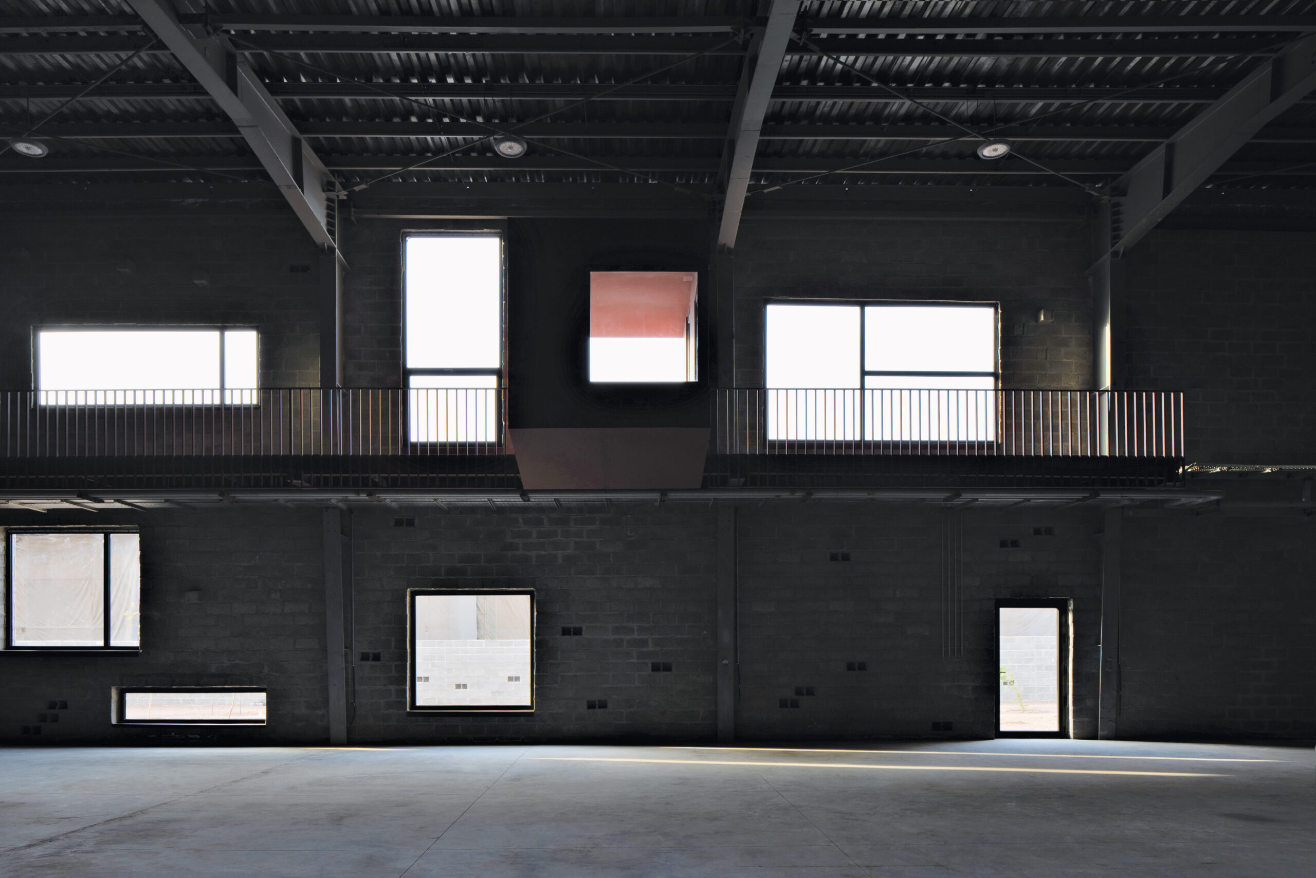 Shadowy factory interior with illuminated windows and doors, stone walls and concrete floors.