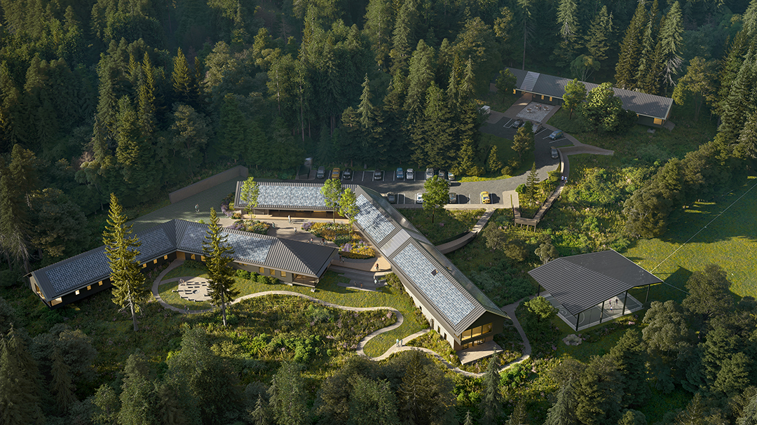 Aerial view of a modern building complex with solar panels, surrounded by dense forest and several cars parked near the structures.