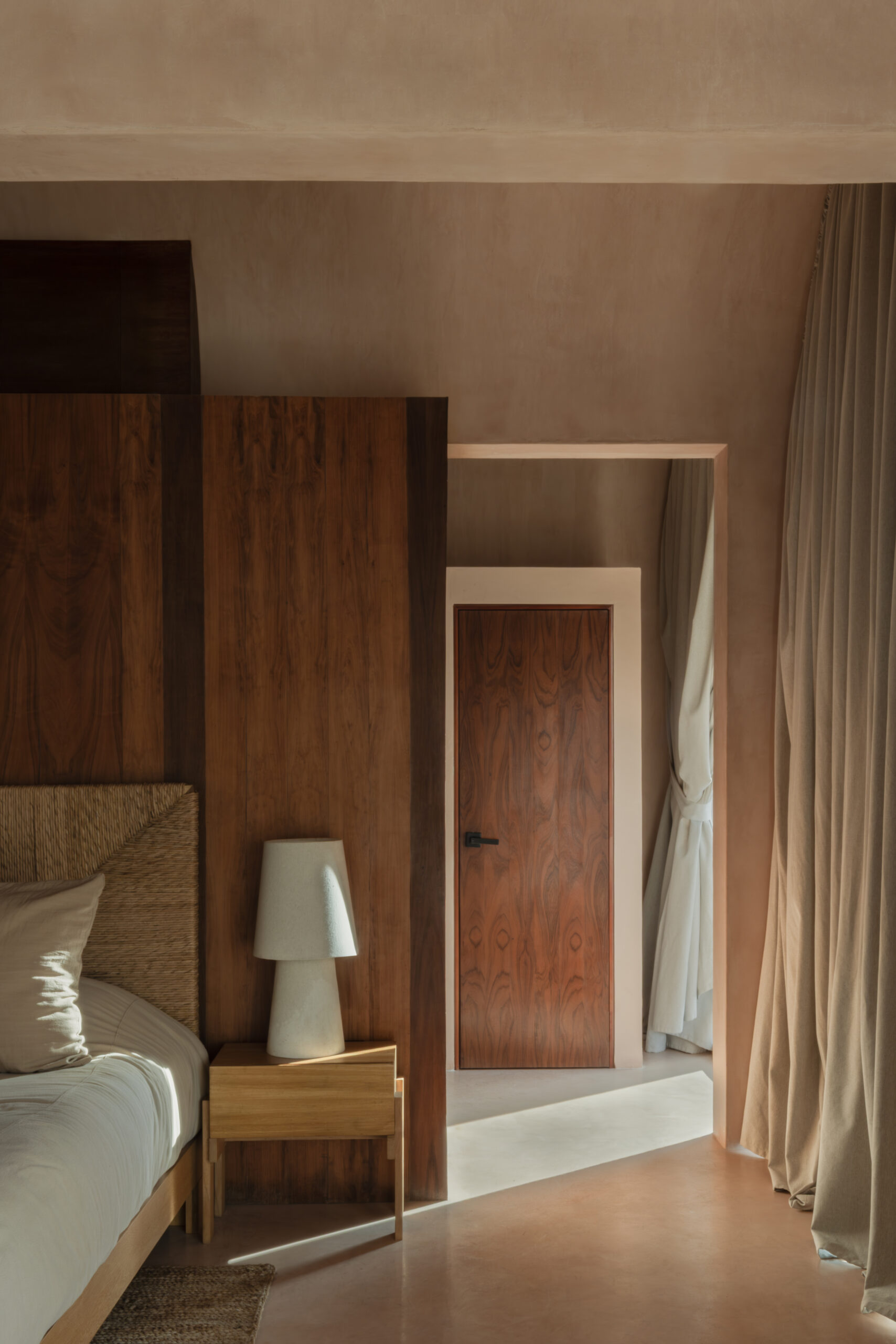Detail shot of modern bedroom interior by V Taller in earth tones with wood accents, white table lamp and drapery. 