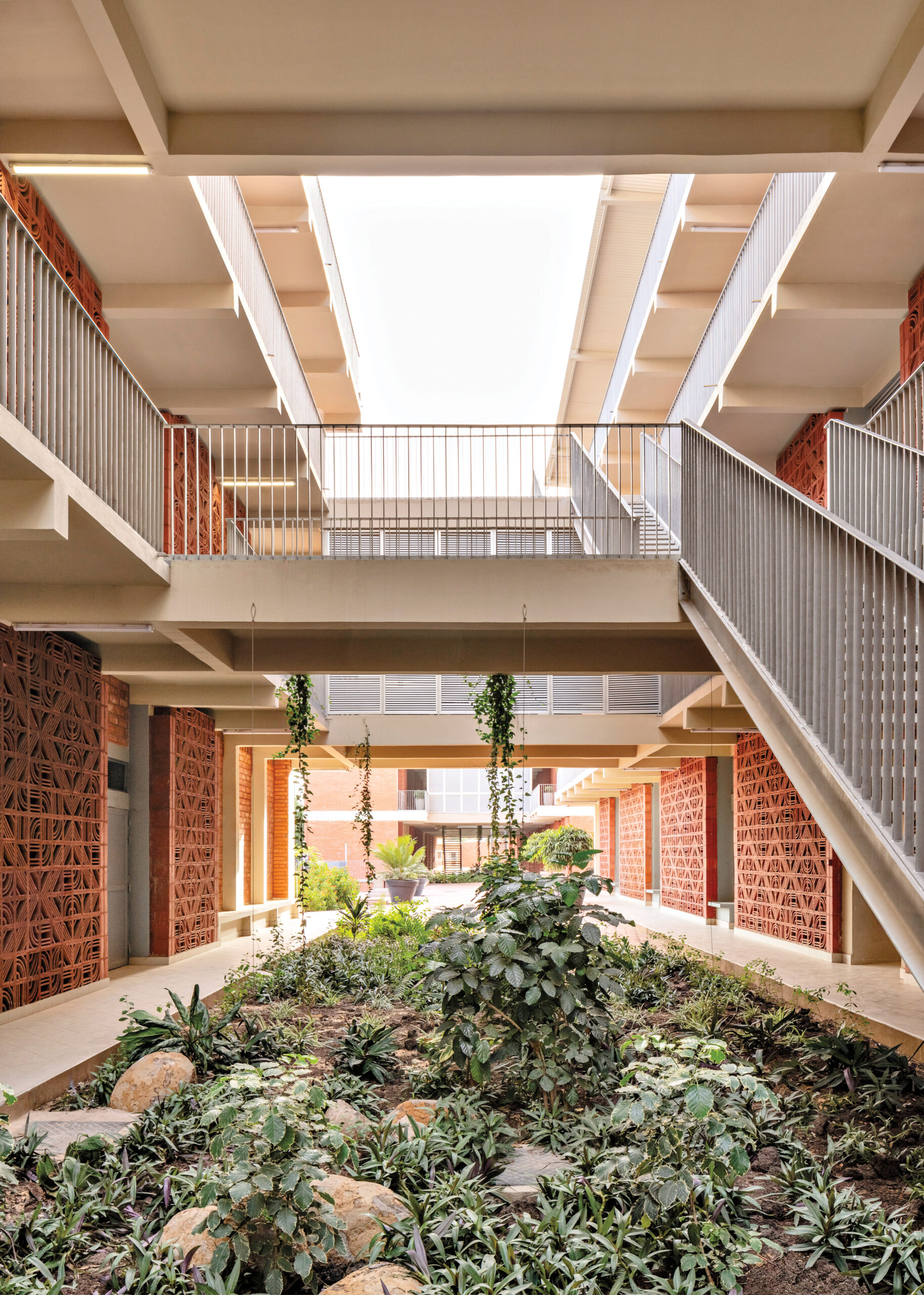 In Dakar, a student housing unit with a central courtyard featuring lush vegetation underneath a cross bridge and terracota brick walls.