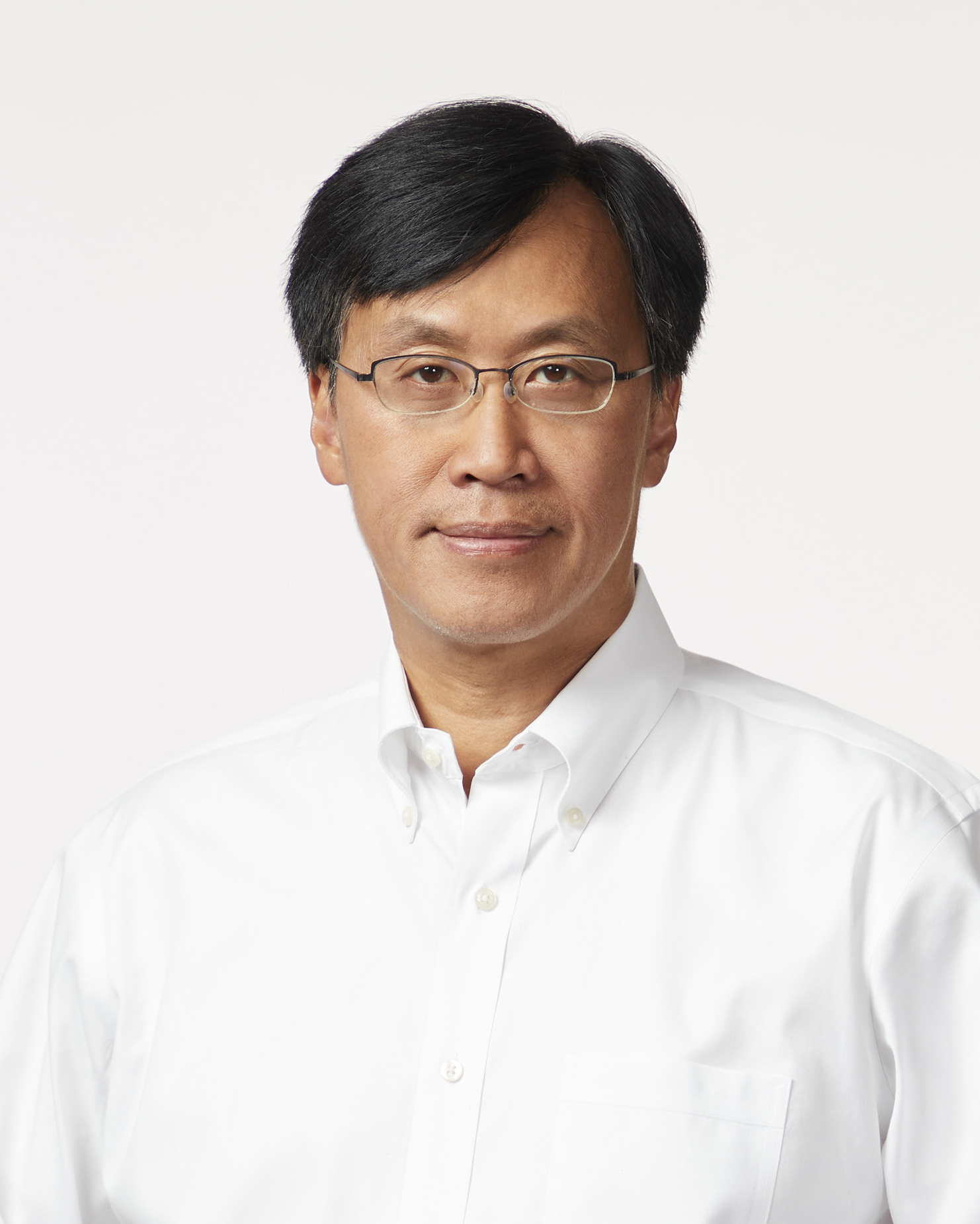 A man with short black hair, glasses, and a white button-down shirt looks at the camera against a plain light background.