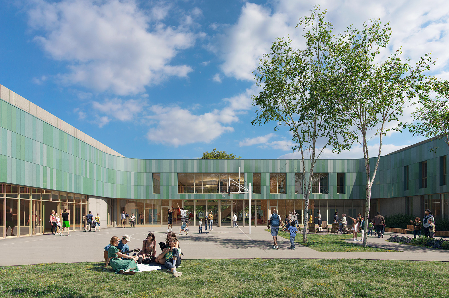 Students gather and relax on the grass and walkways outside a modern, two-story school building with green exterior panels and large windows under a partly cloudy sky.