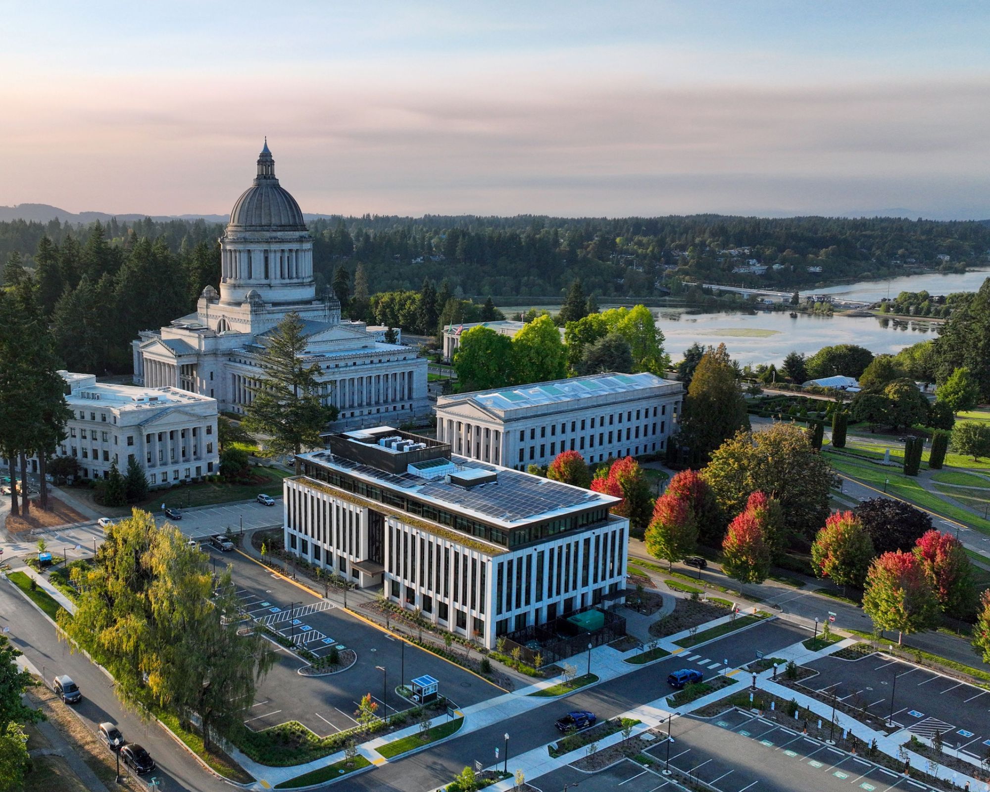 Aerial view of the Washington State Capitol campus with government buildings, trees, parking lots, and a river in the background.