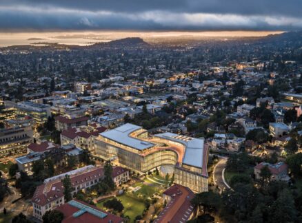 Aerial view of the curved, multi-story Lucas Museum of Narrative Art illuminated at twilight, situated within a city and neighborhood landscape.