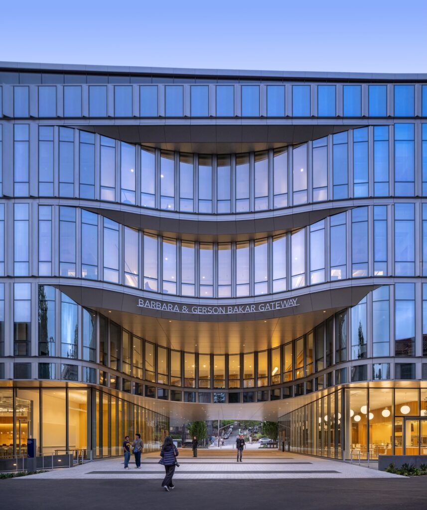 The Barbara & Gerson Bakar Gateway building, part of the Lucas Museum of Narrative Art, features a multi-story glass facade and a central recessed entryway with pedestrians walking beneath.