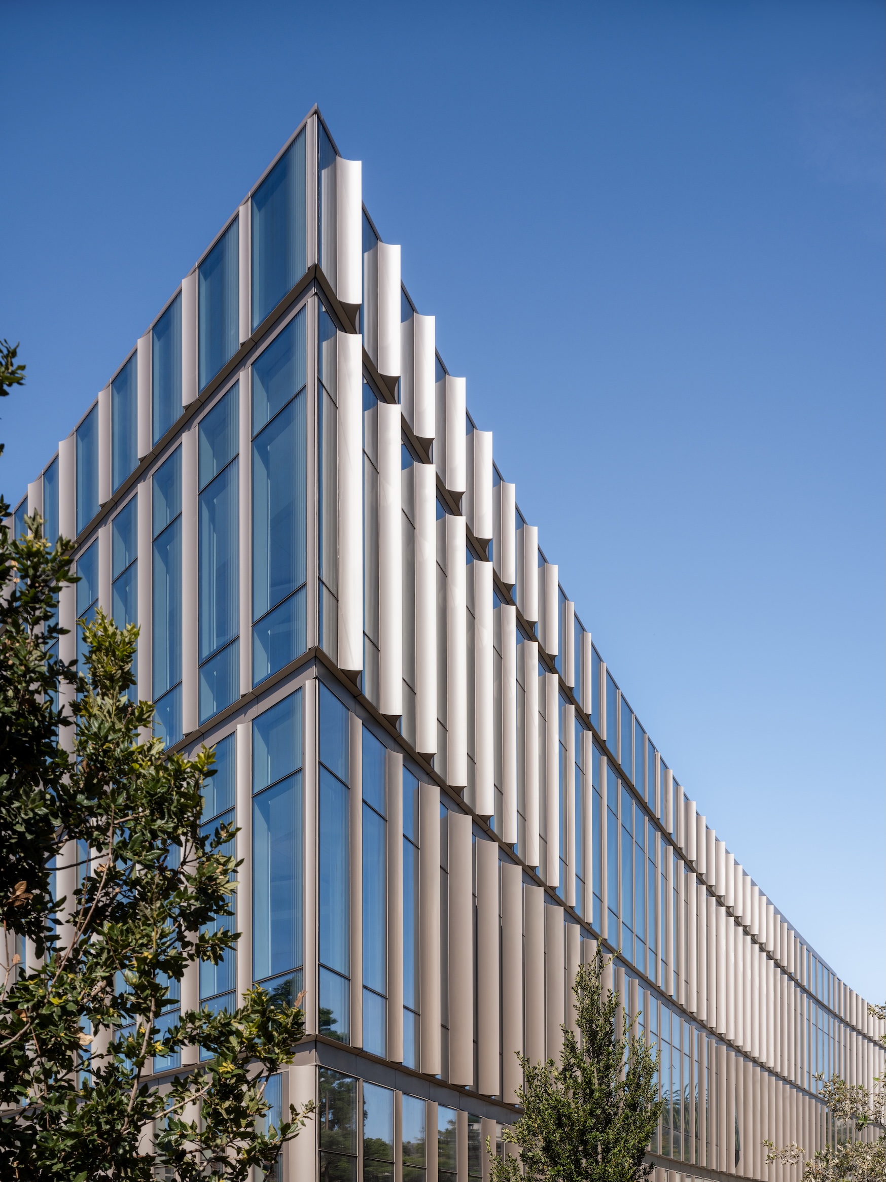 Modern glass facade of the Lucas Museum of Narrative Art with vertical sun-shading fins set against a clear blue sky.