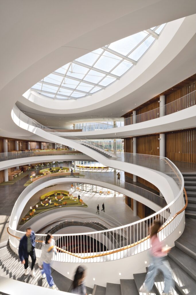 The Lucas Museum of Narrative Art features a multi-story atrium with a central spiral staircase, a large circular skylight, and several people walking along the curved balconies.