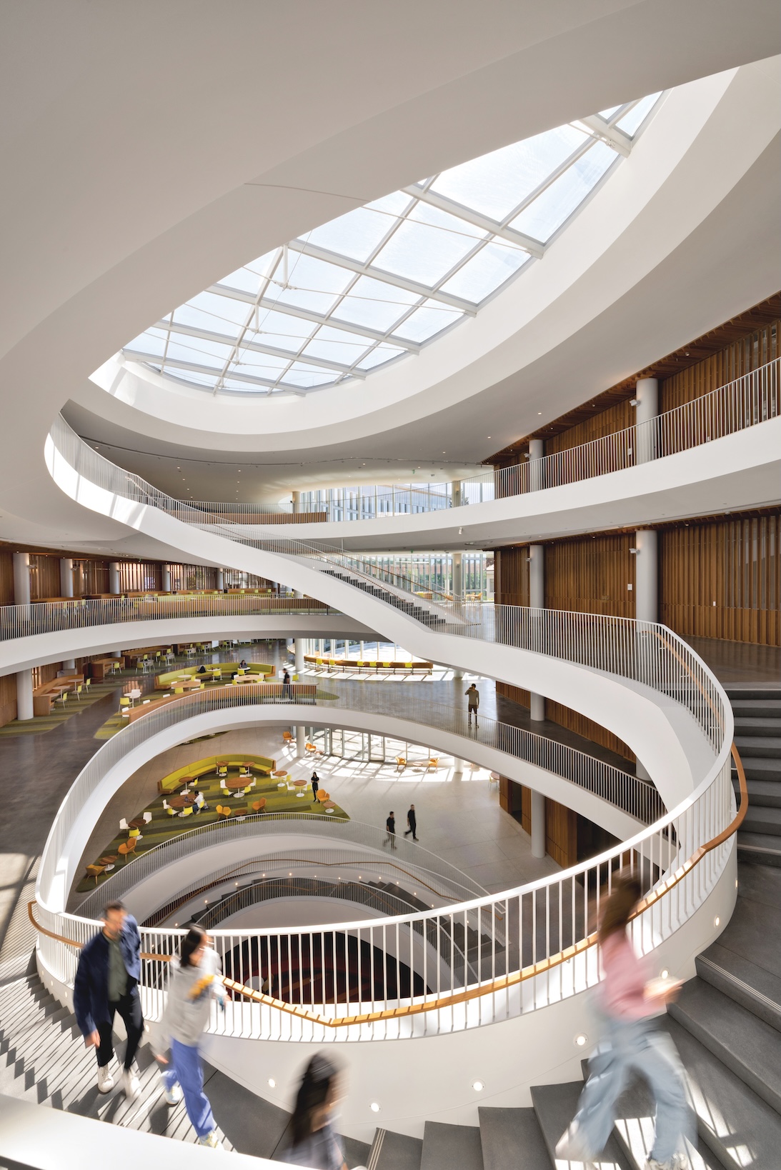 The Lucas Museum of Narrative Art features a multi-story atrium with a central spiral staircase, a large circular skylight, and several people walking along the curved balconies.