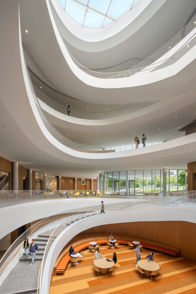 An expansive, multi-level atrium at the Lucas Museum of Narrative Art featuring a curved white staircase, curved balconies, and a circular skylight above a ground-floor seating area.