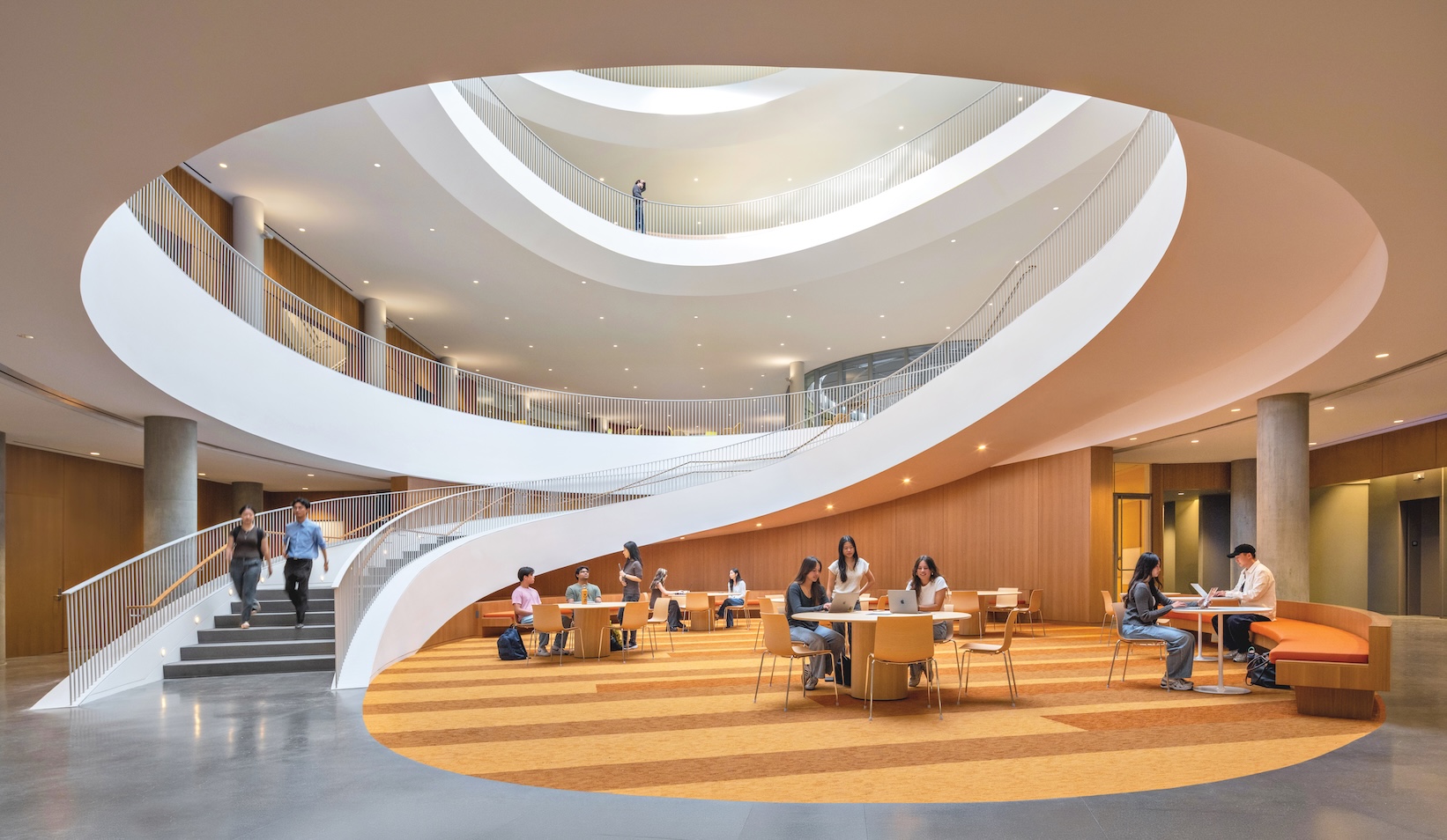 Students study at tables in a large, modern atrium at the Lucas Museum of Narrative Art, featuring a central circular staircase and open levels.