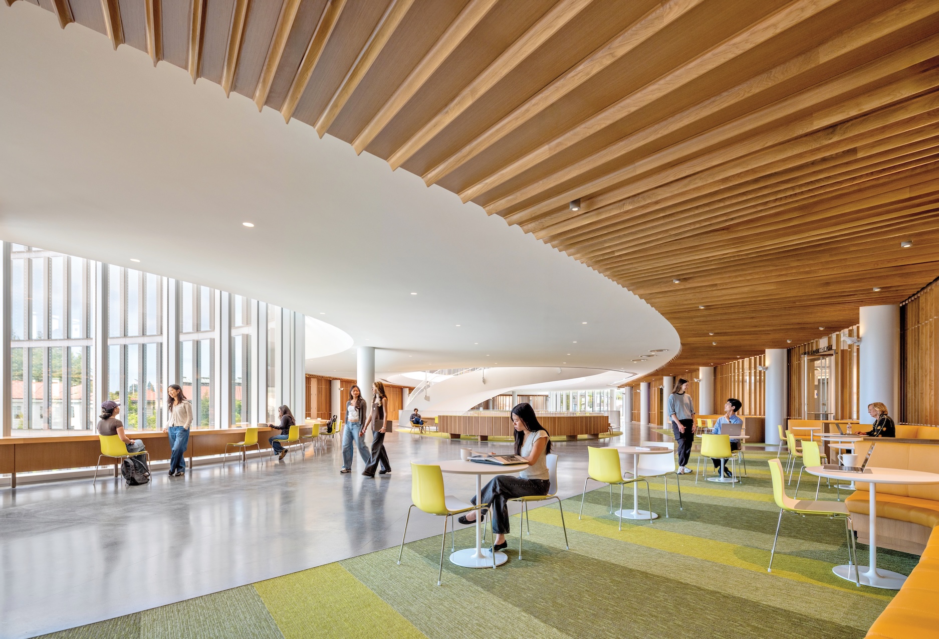 Students study and walk through the Lucas Museum of Narrative Art, a modern space with floor-to-ceiling windows, yellow chairs, and curved wooden slat ceilings.