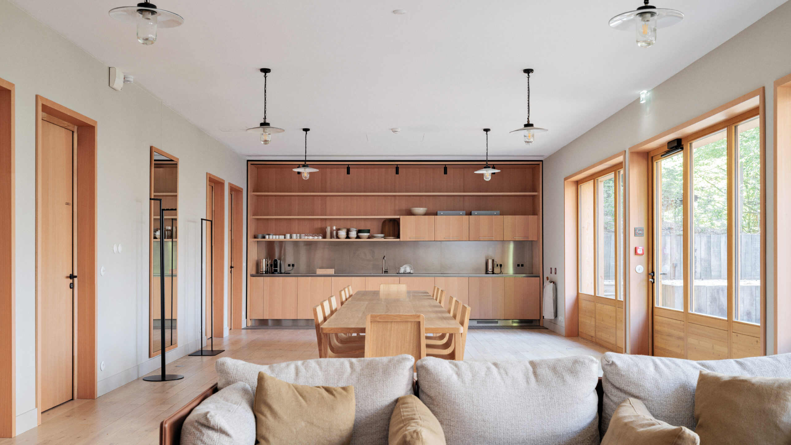 Modern interior with wood finishes, a central dining table, white couch, and large windows.