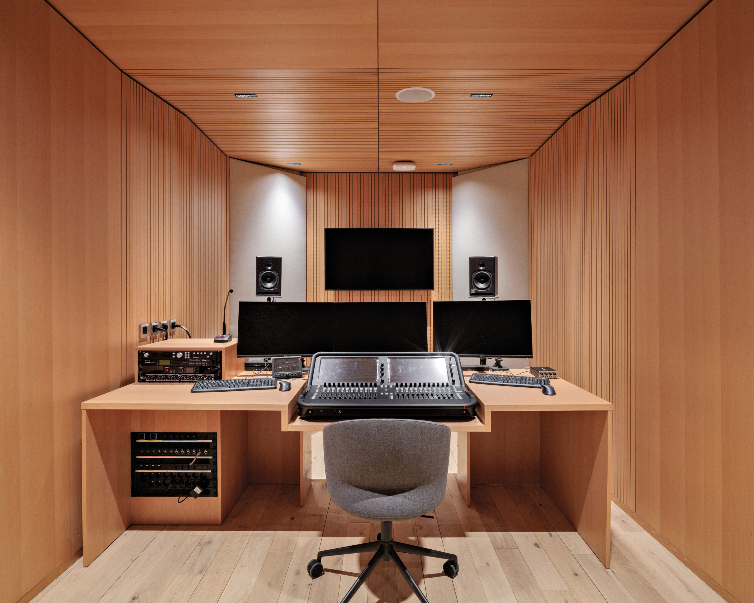 A modern recording booth wrapped in warm wood with a desk and console.