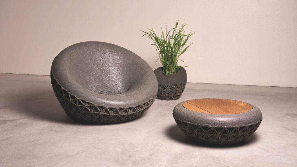 A gray lounge chair by Common Object Studio, a matching planter with a green plant, and a round coffee table with a wooden top, all featuring a textured lattice base.