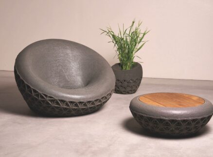 A gray lounge chair by Common Object Studio, a matching planter with a green plant, and a round coffee table with a wooden top, all featuring a textured lattice base.