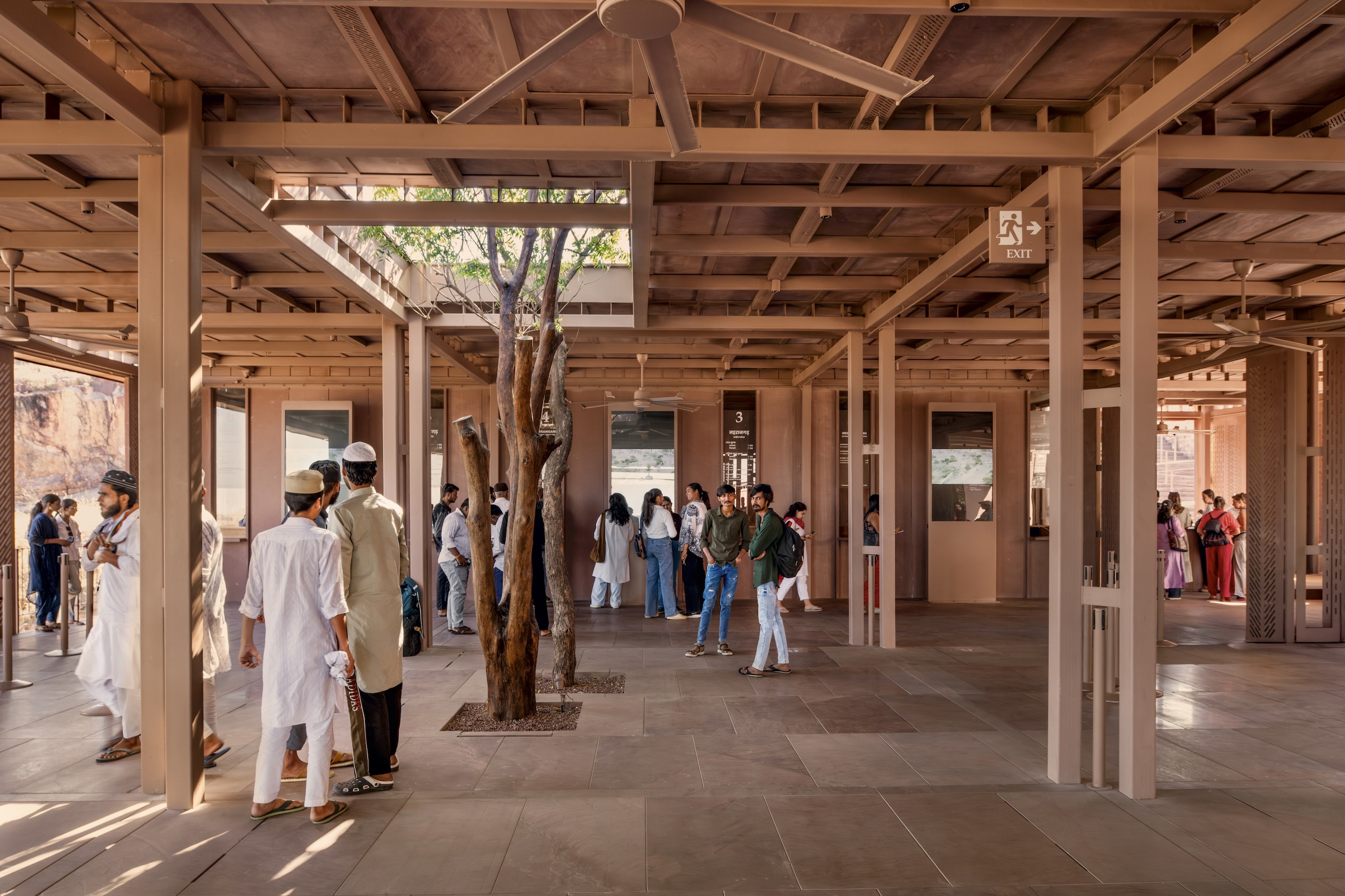 People stand in The Barbara and Gerson Bakar Gateway at UC Berkeley, an open-air pavilion with a metal beamed ceiling and a tree growing through the floor.