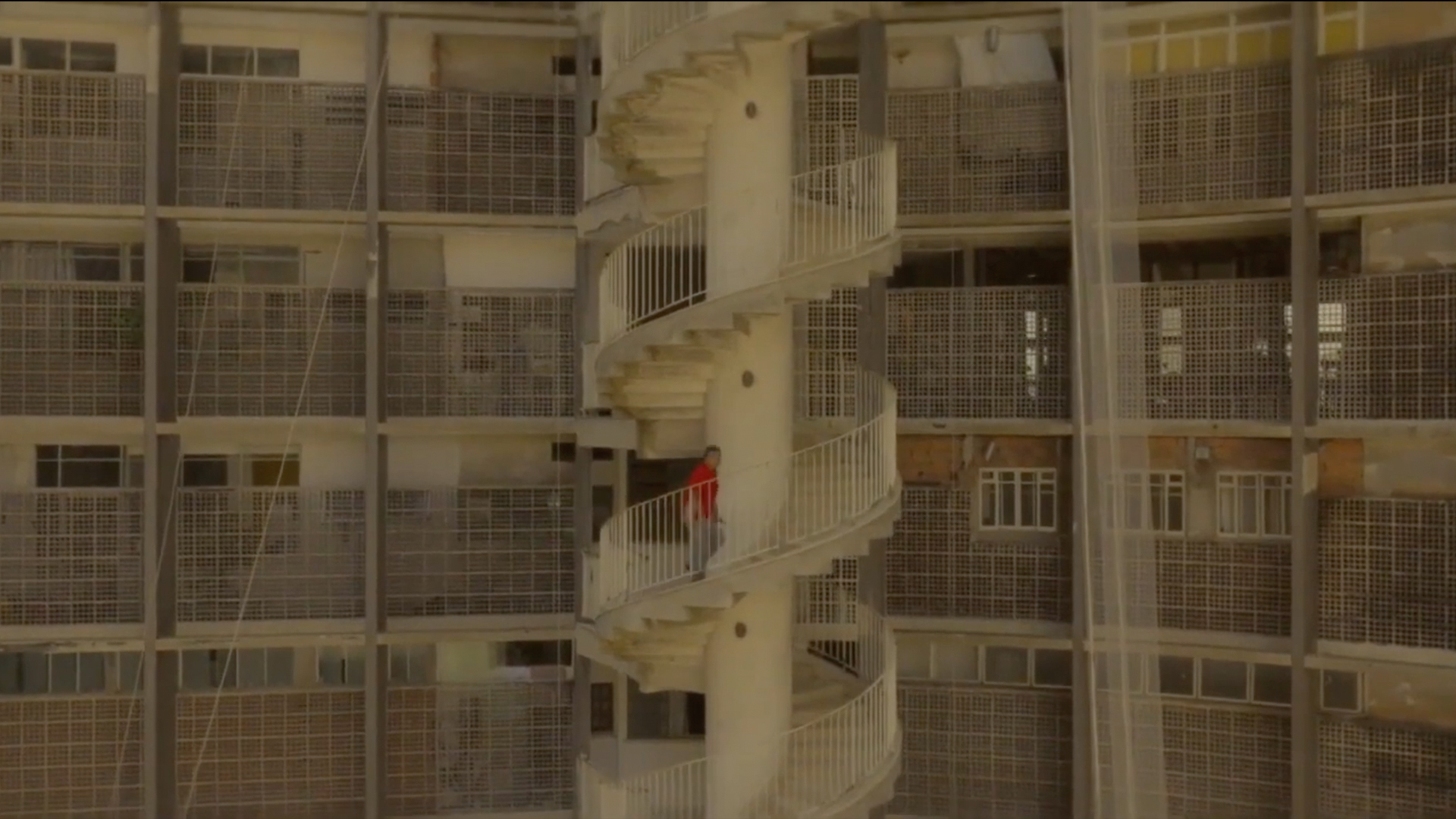 A person in a red shirt walks up an outdoor spiral staircase on a gridded concrete building during Archtober 2026.