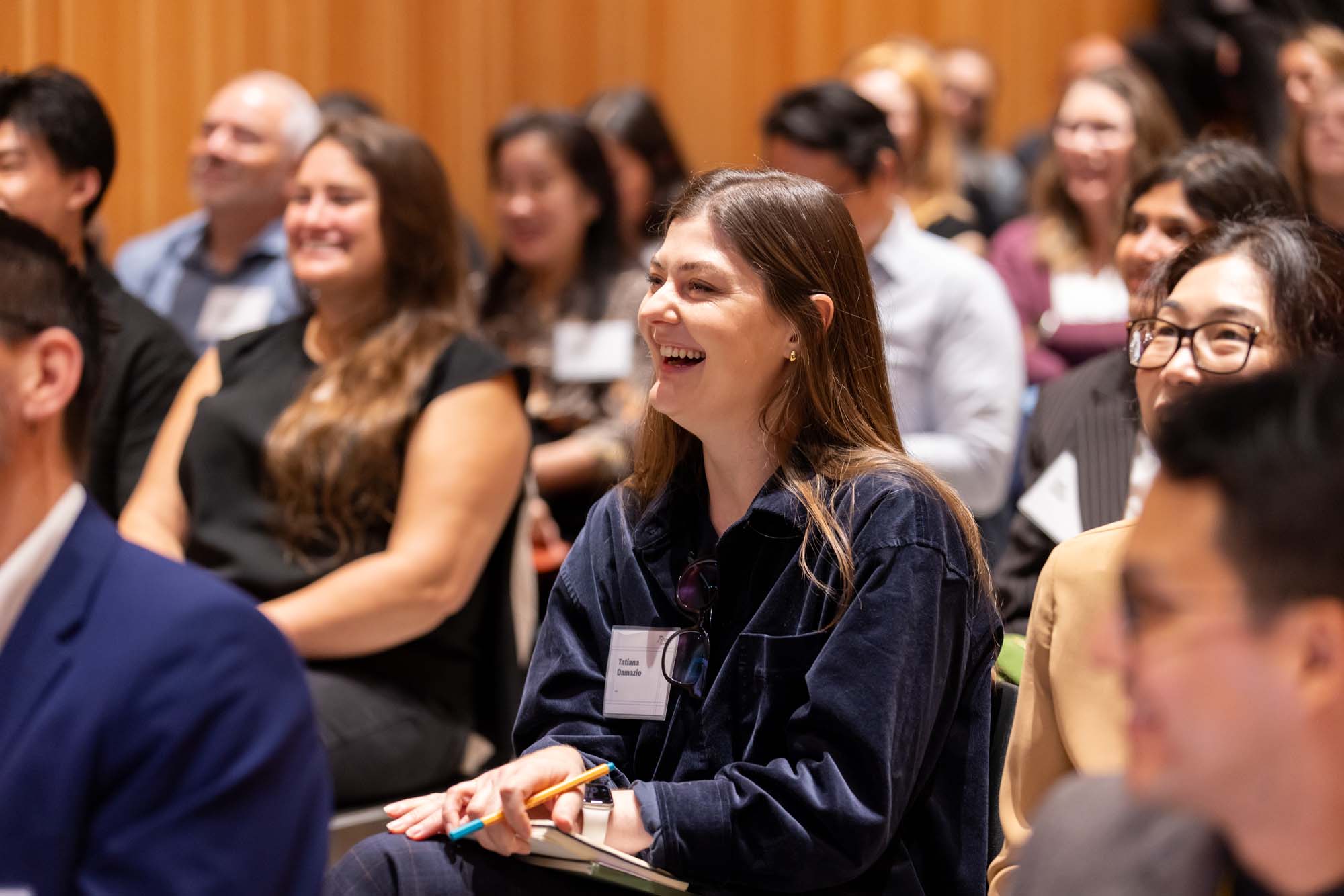 A woman laughing in an audience at an indoor event.