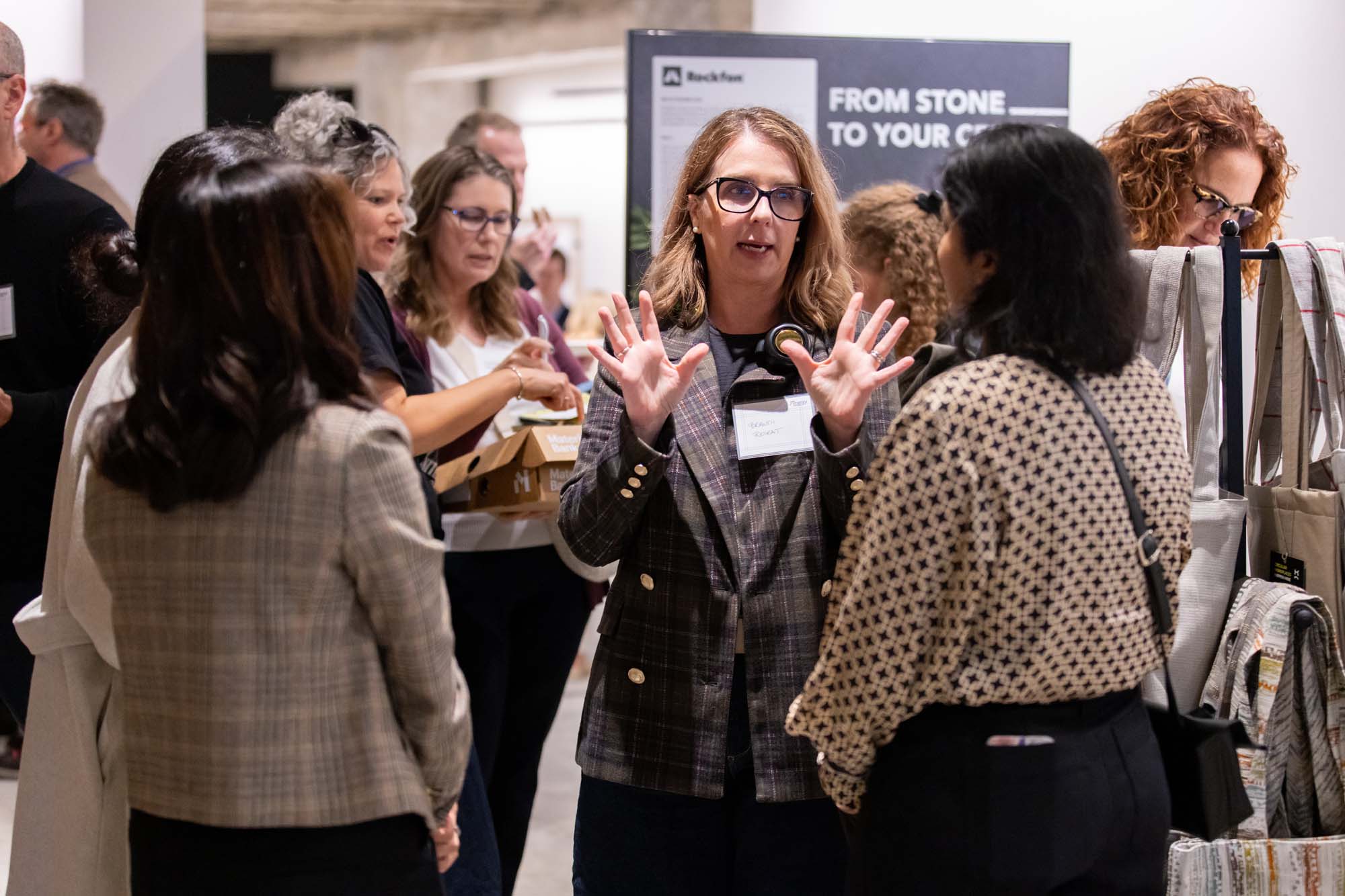 A woman in a plaid blazer gestures with her hands while speaking to a group at a professional event.