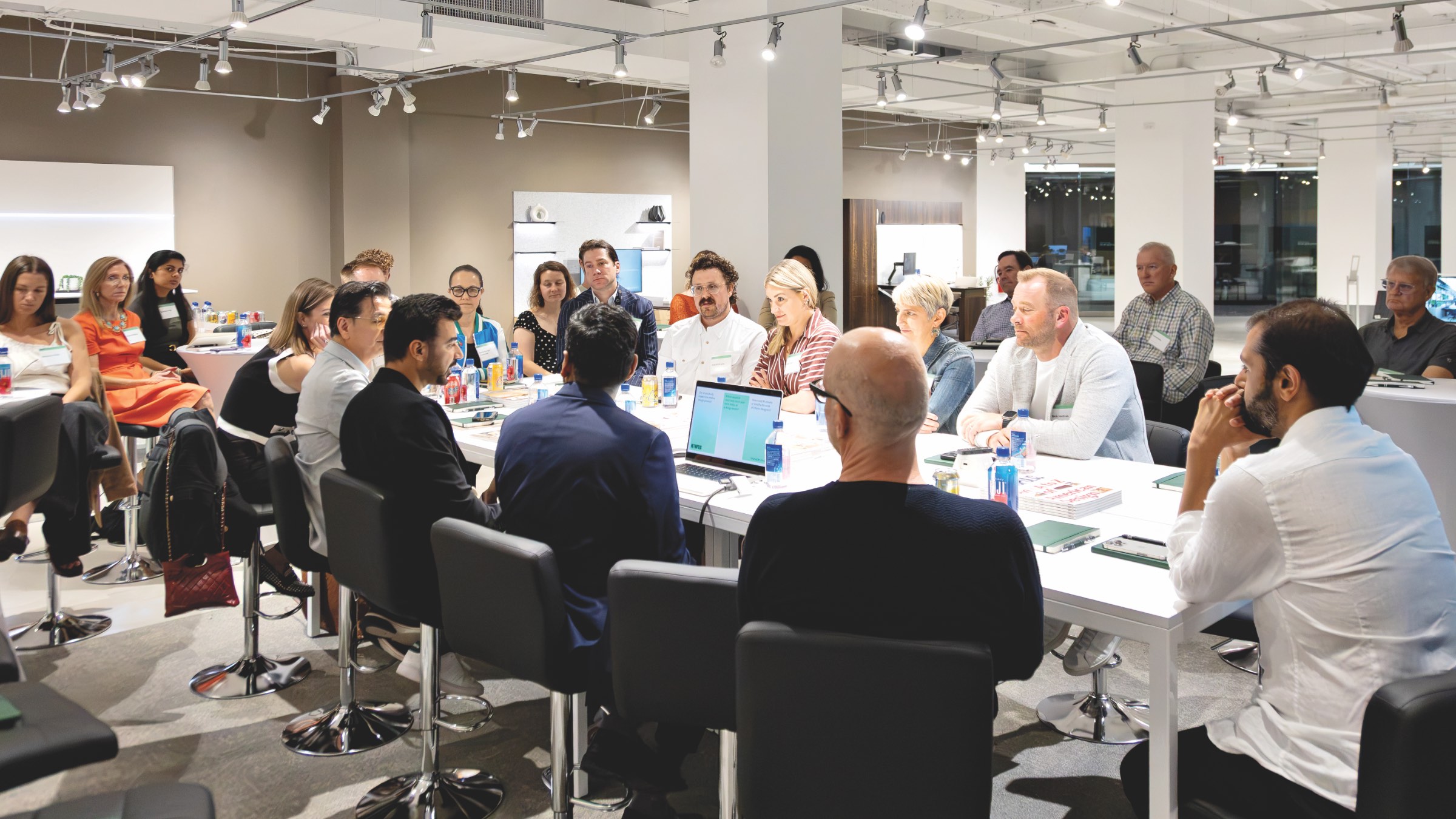 Designers AI: A group of people seated around a long white table in an office space, engaged in a discussion.
