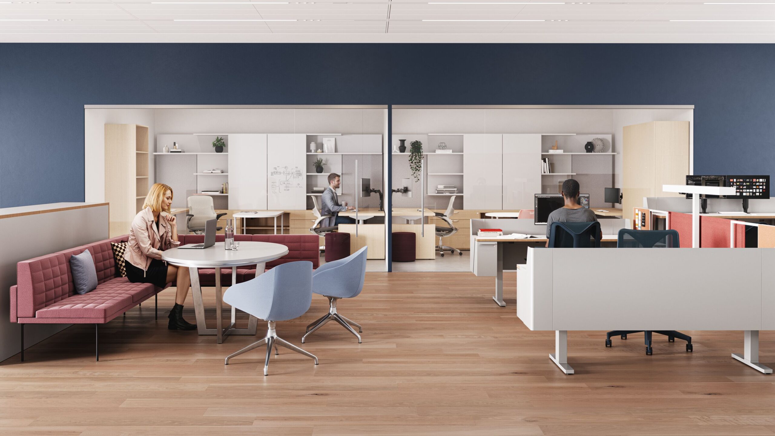 An open-plan office space featuring a pink sofa with a round table, individual workstations, and employees working at computers.