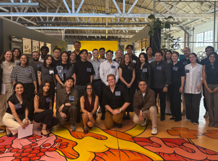 A large group of Arch30 team members posing for a photo in a warehouse-style office space with a decorative painted floor.
