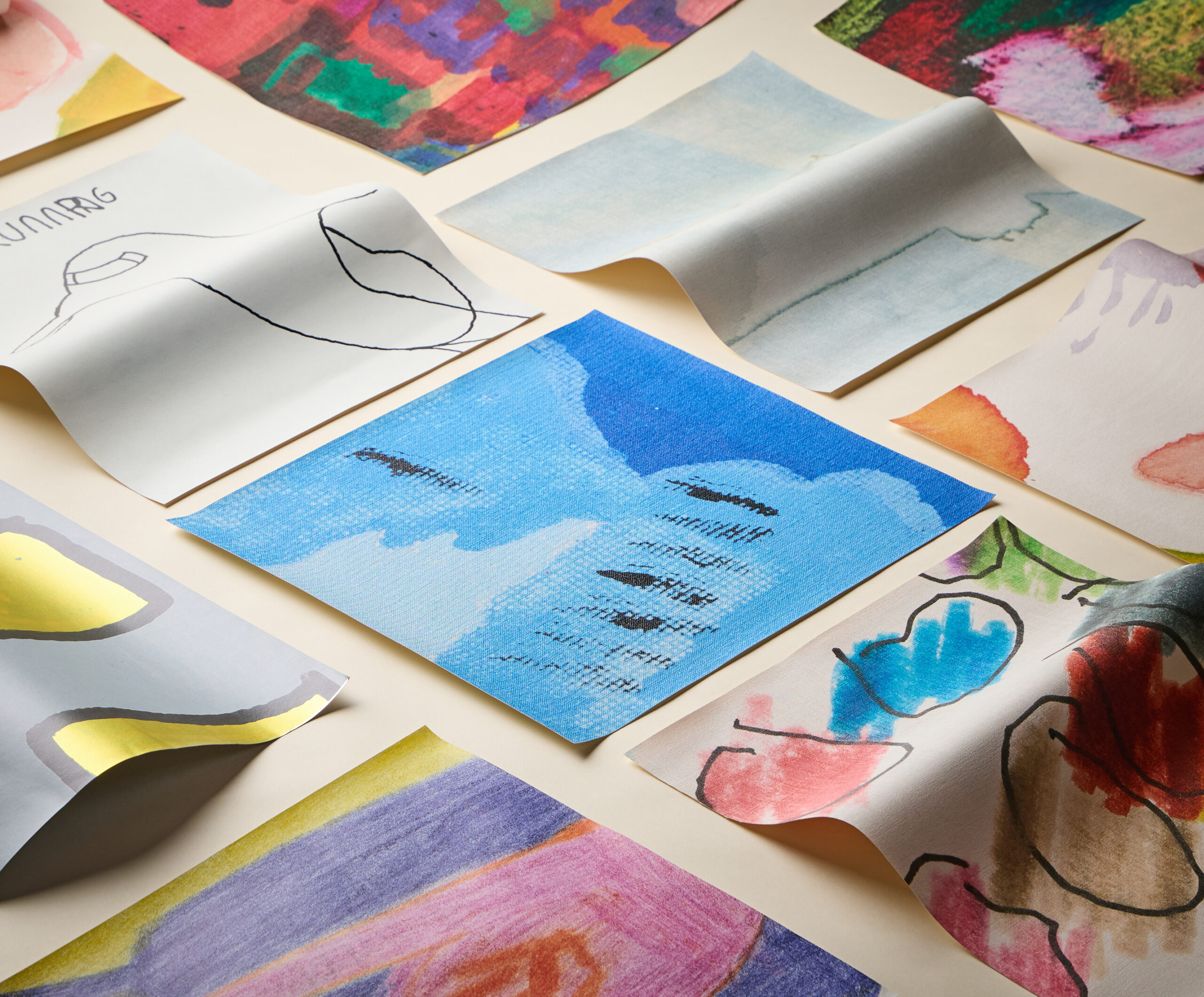 An assortment of square papers with colorful abstract drawings, sketches, and watercolor paintings arranged to capture creative momentum on a light surface.