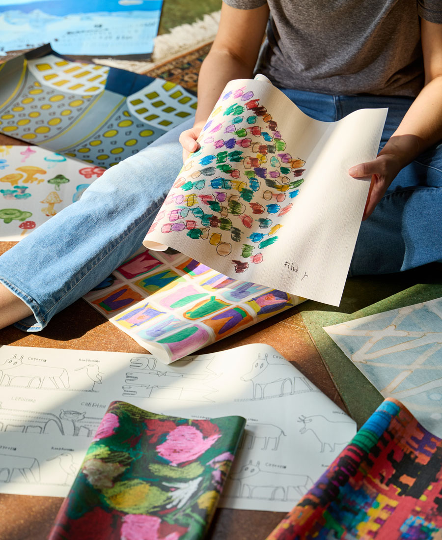 A person sitting on the floor surrounded by several sheets of hand-drawn and painted artwork.