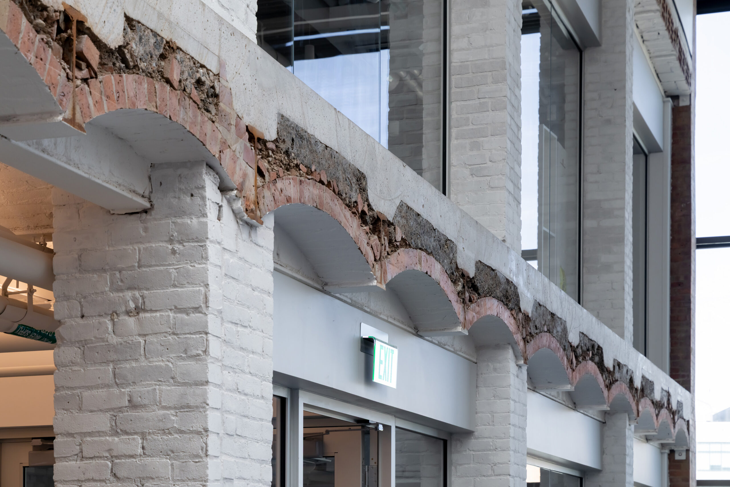 Exposed brick arches supported by white painted brick columns above an exit sign in a modern MIT Future Fest office space.