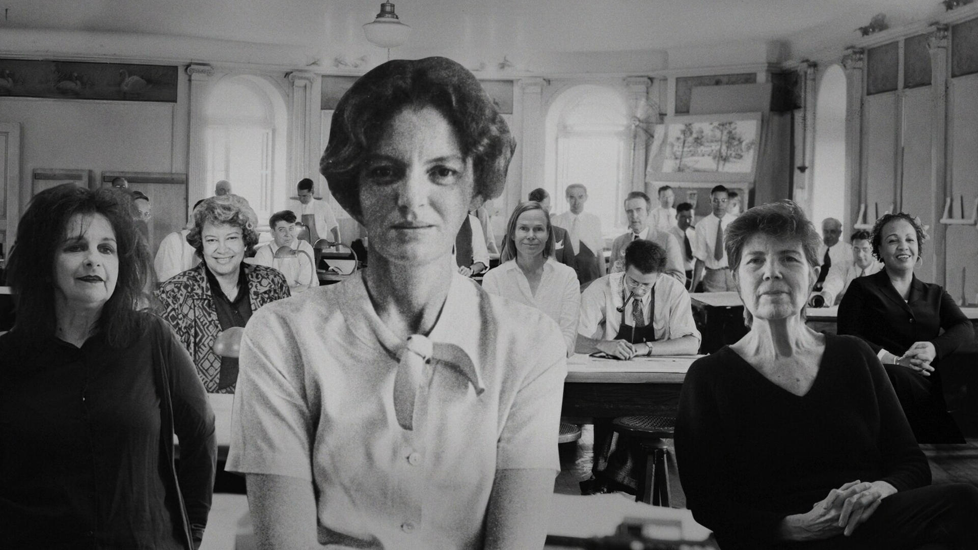 A black-and-white photo of a group of people sitting at desks in a classroom, with three women in the foreground, captured during Archtober 2026.