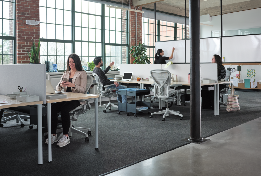 People working in a modern open-plan office with brick walls and large windows.
