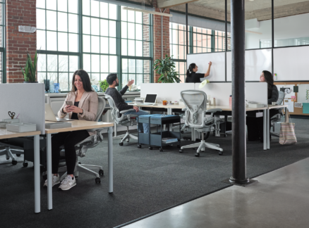 People working in a modern open-plan office with brick walls and large windows.
