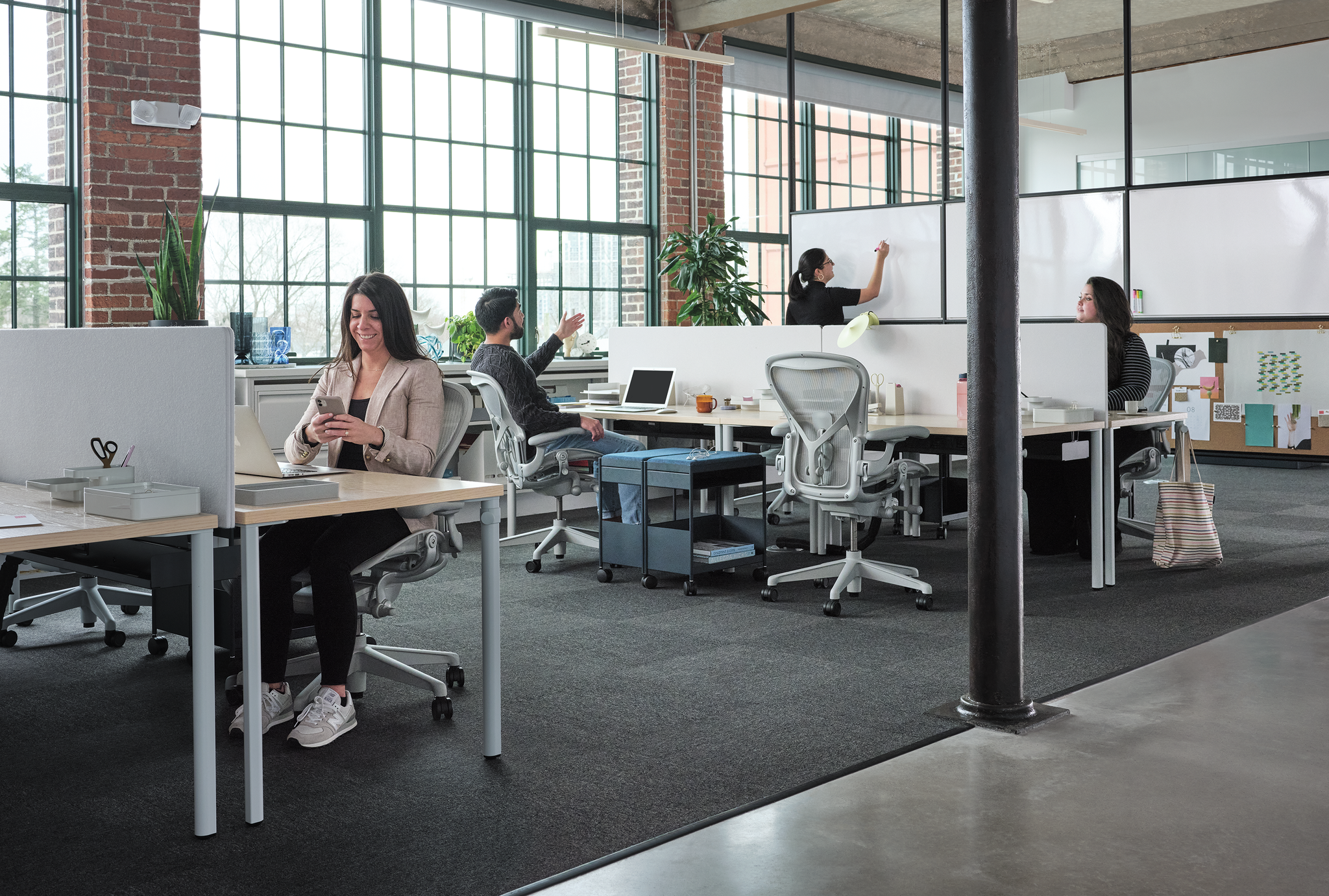 People working in a modern open-plan office with brick walls and large windows.