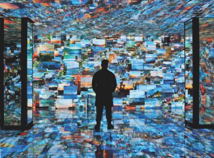 A person stands in a room surrounded by a digital projection of numerous landscape photographs covering the walls, ceiling, and floor.