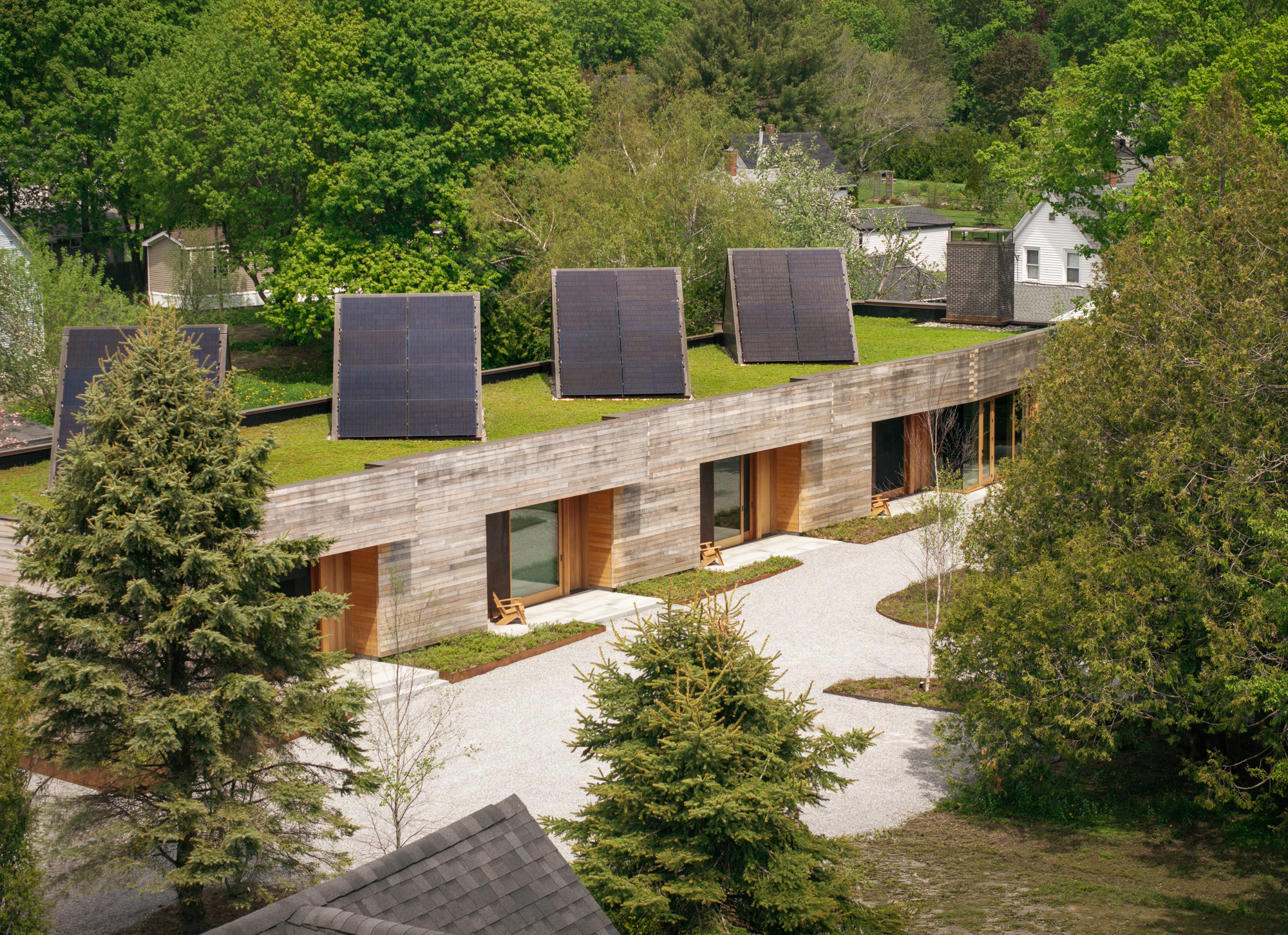 A long, modern Ellis-Beauregard Foundation house with a green roof, solar panels, and a light-colored gravel courtyard.