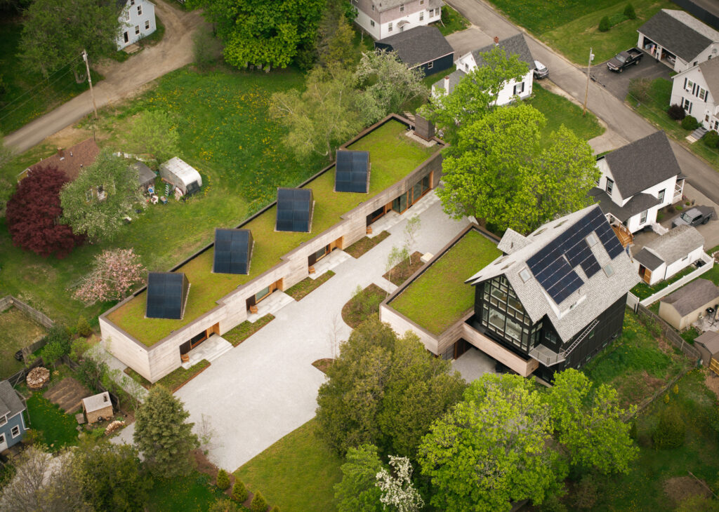 Aerial view of a residential property featuring two modern buildings with green roofs and solar panels, surrounded by a gravel driveway and lawn.