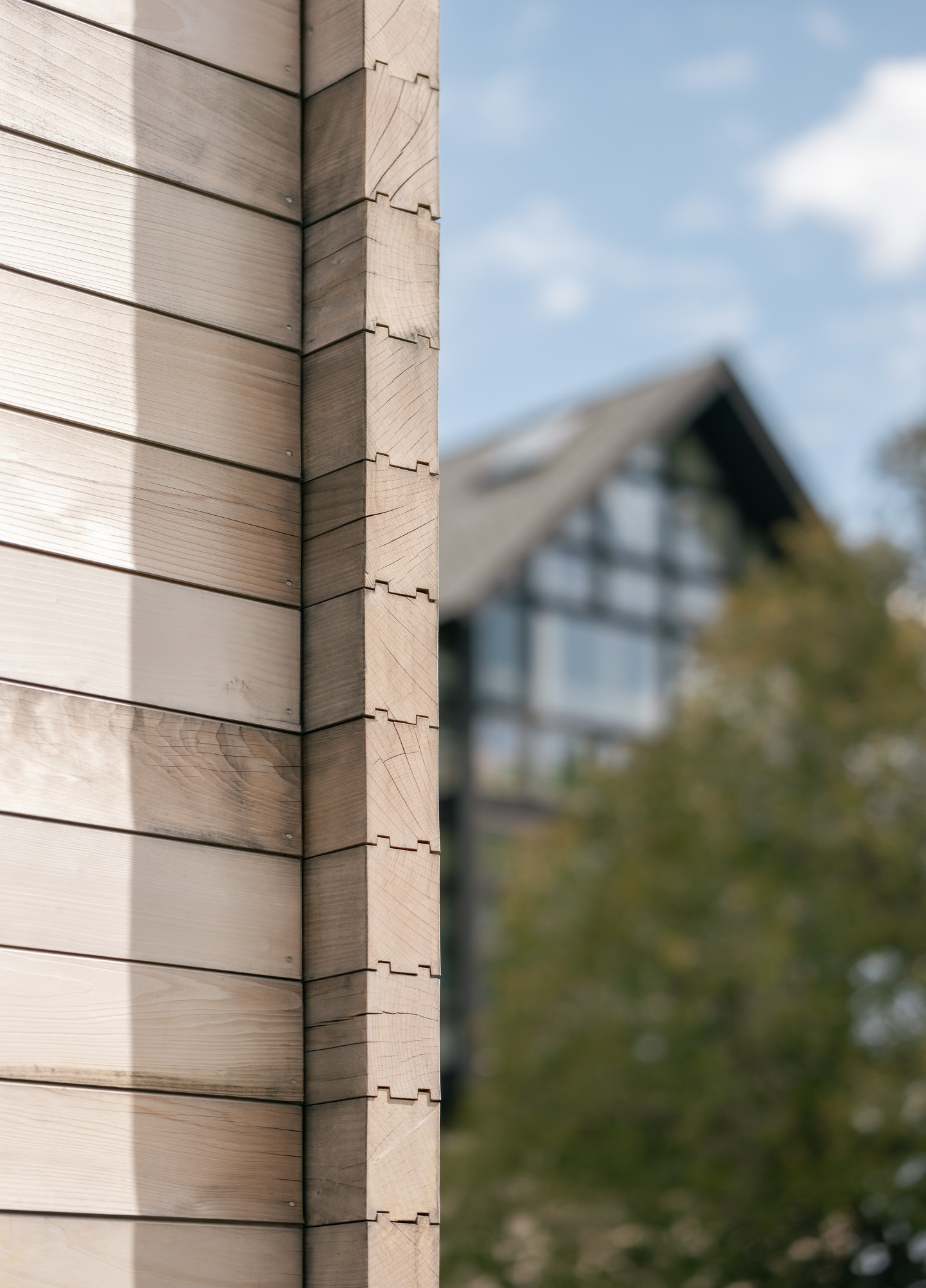 A close-up of a finger-jointed wooden wall corner at the Ellis-Beauregard Foundation, with a blurred house in the background.