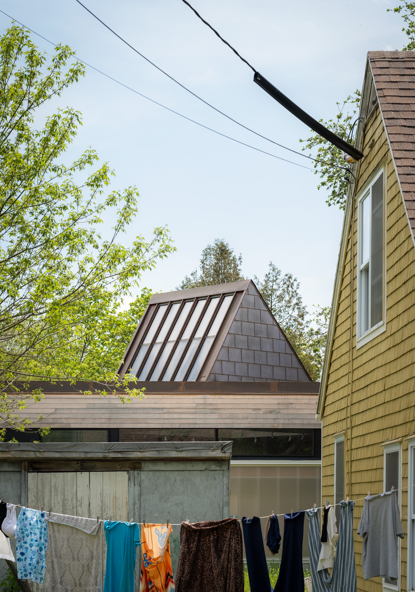A yellow-shingled house with a clothesline in the foreground stands before a modern, glass-roofed structure at the Ellis-Beauregard Foundation.