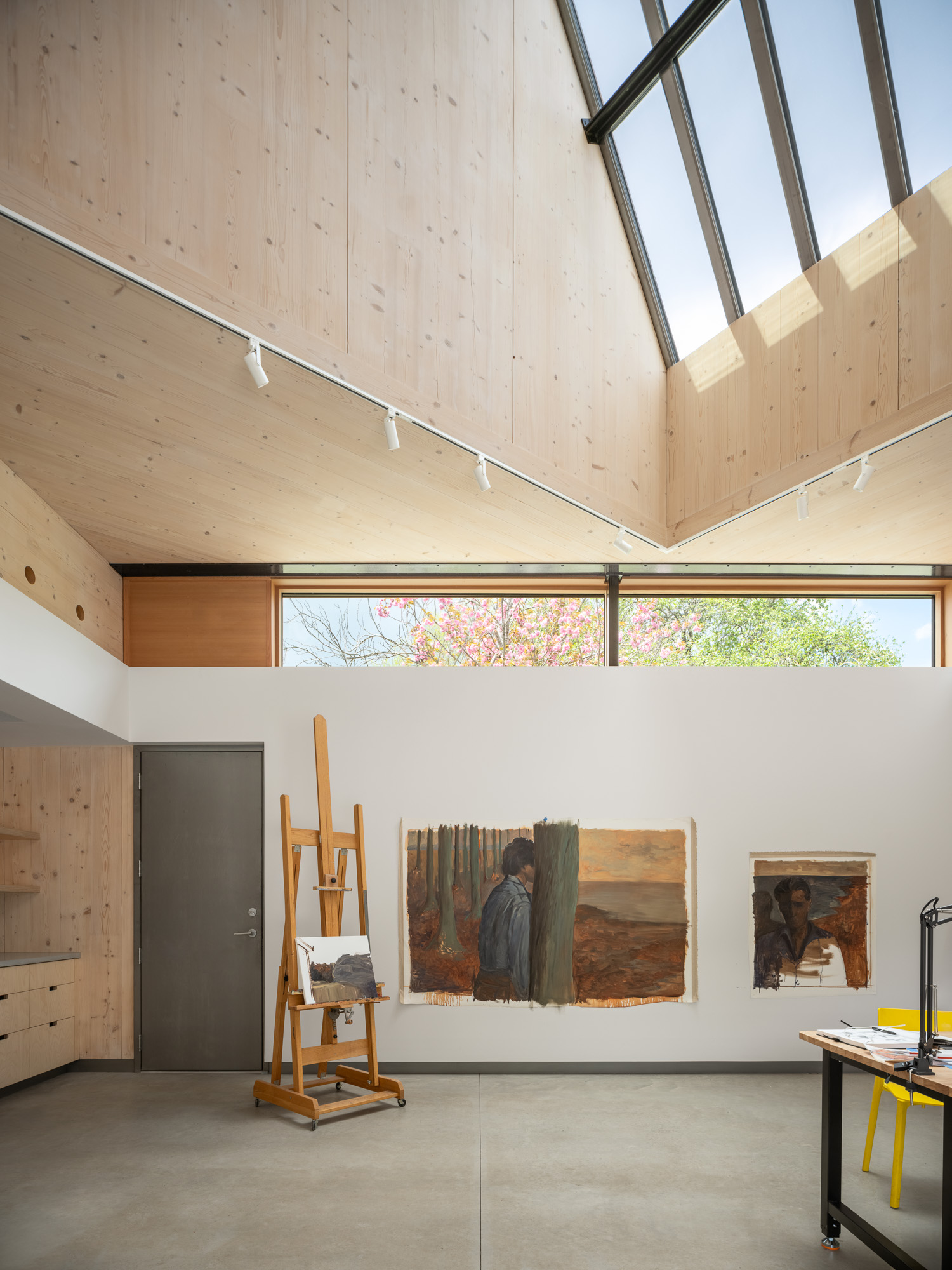 An artist’s studio at the Ellis-Beauregard Foundation with light wood walls, a skylight, and paintings hanging on a white wall near an easel.