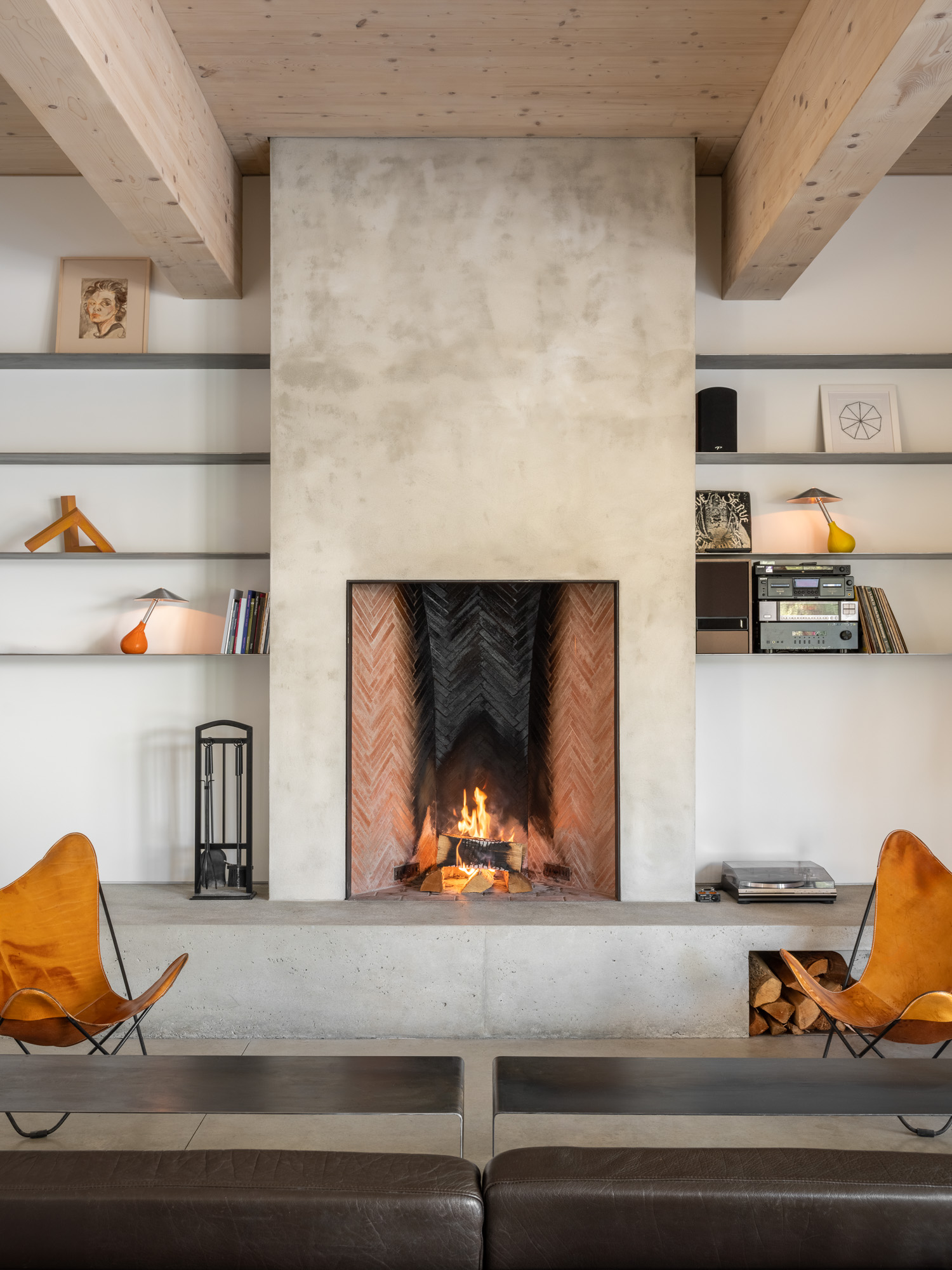 A fireplace with a burning fire at the Ellis-Beauregard Foundation, flanked by open shelving and two leather butterfly chairs.