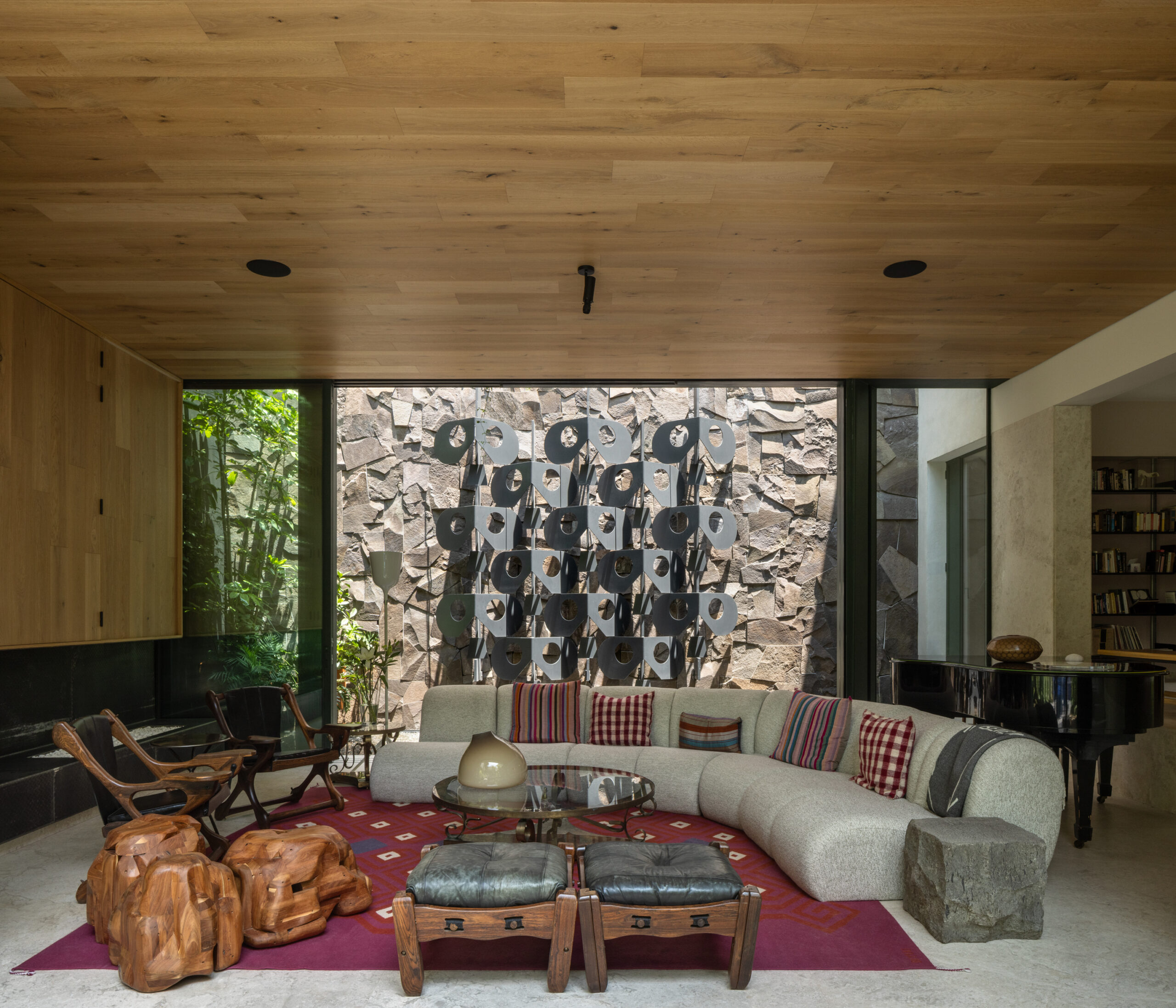 A modern living room with a curved sofa, a geometric metal wall sculpture visible through a window, and wood-paneled ceilings.