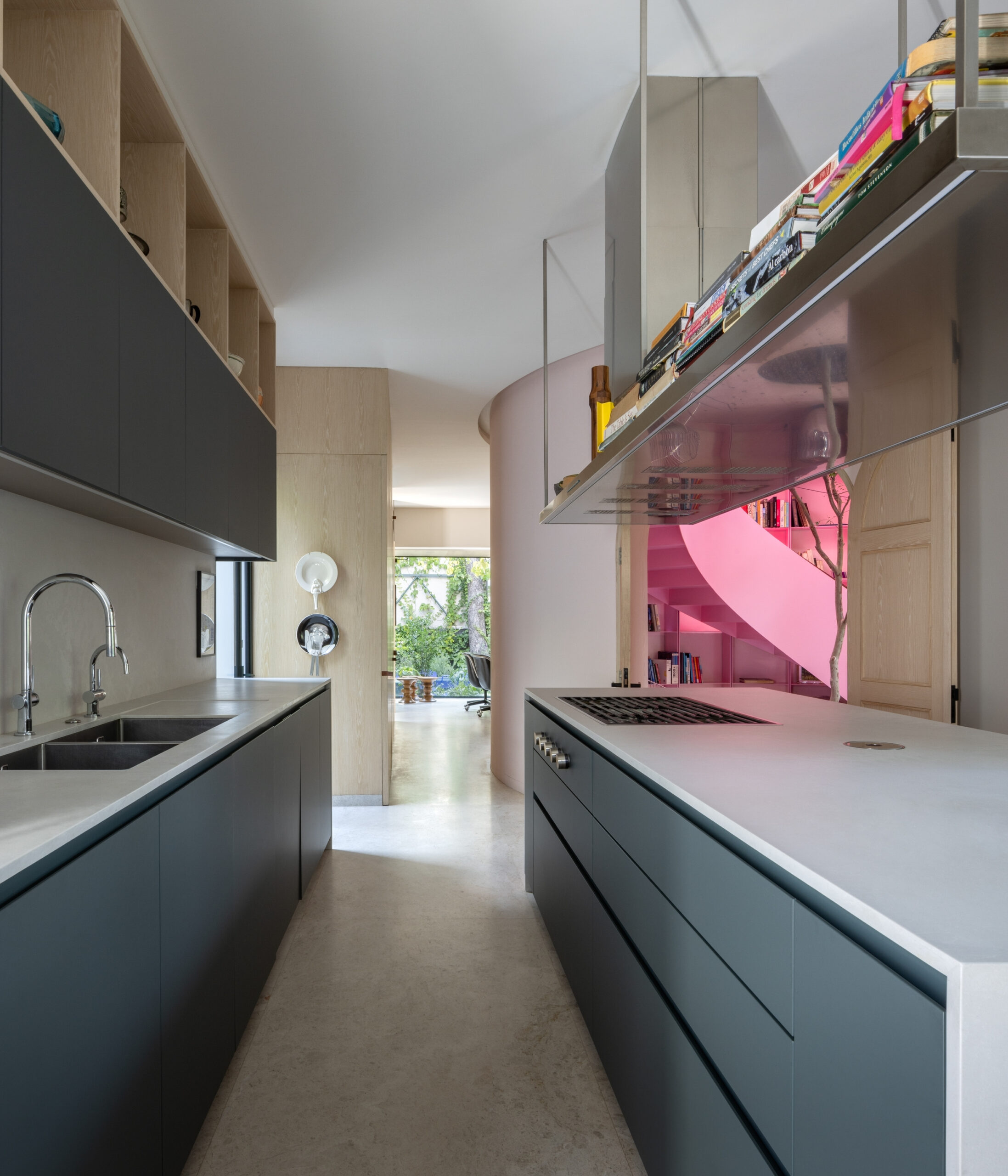A modern galley kitchen with dark cabinets and white countertops, leading to a hallway with a bright pink spiral staircase.