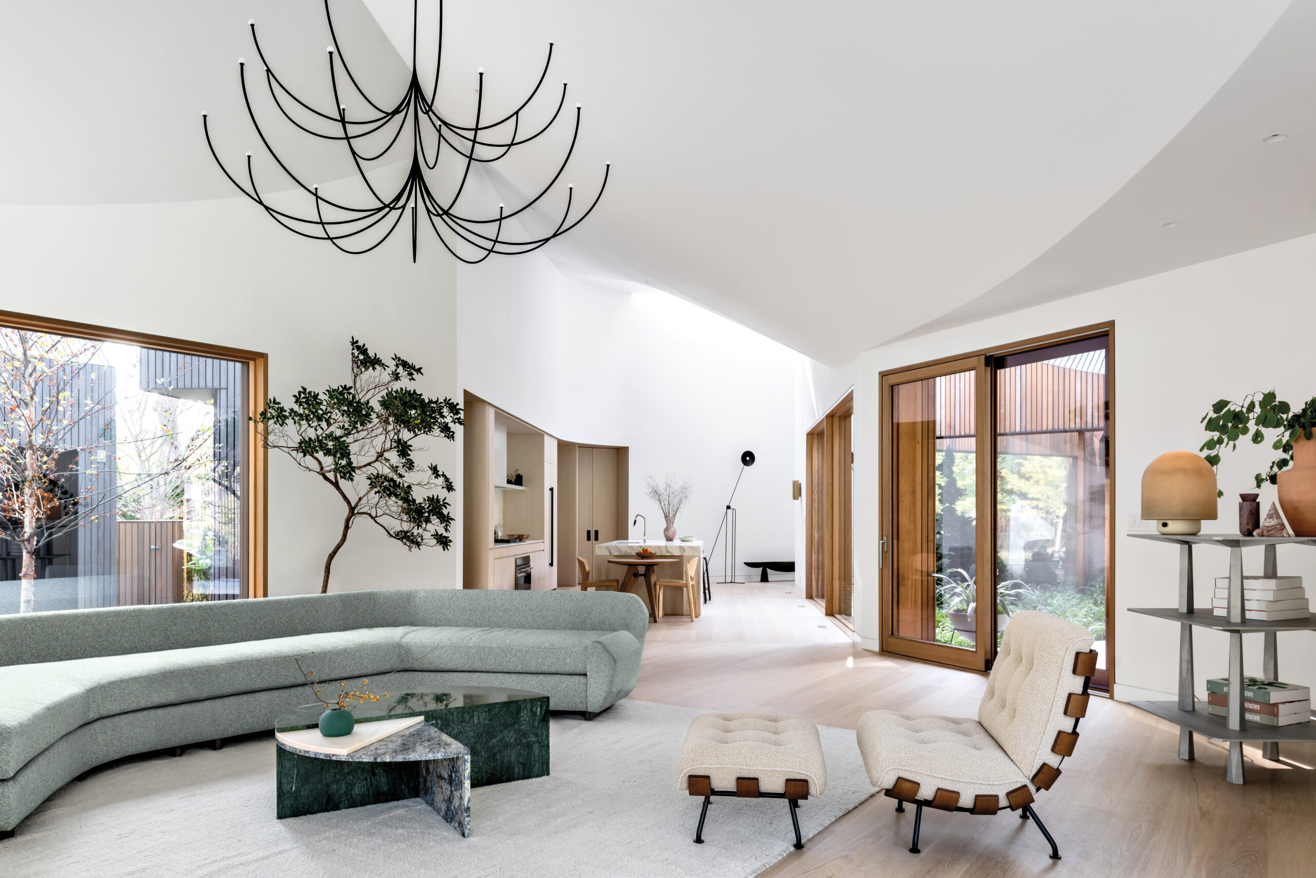 Interiors of the Six Square House by Young Projects. The living room opens onto an interior courtyard and connects directly to the kitchen, creating an open-plan living space beneath a ruled ceiling shaped by the home’s interconnected roof geometry.